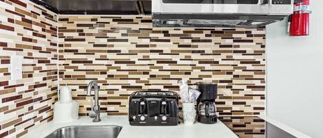 A kitchen with a modern design, featuring a stainless steel sink, a toaster, a coffee maker, and a microwave.