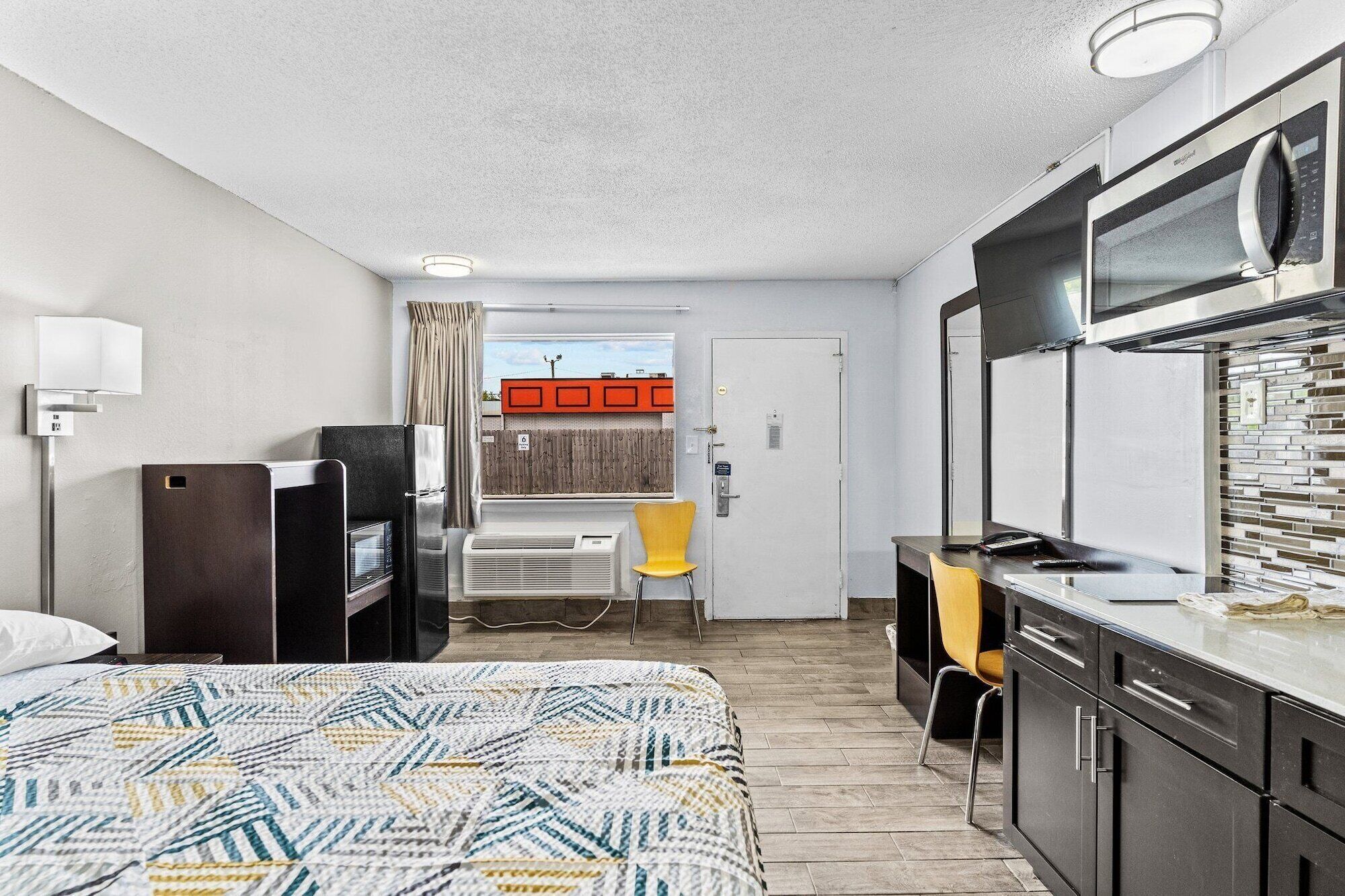 Habitación de hotel compacta con cama, kitchenette y un pequeño escritorio.