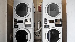 Two stacked front-loading washing machines in a laundry room with a sign indicating the laundry center is open. - Studio 6 Wilmington, NC (Wilmington)
