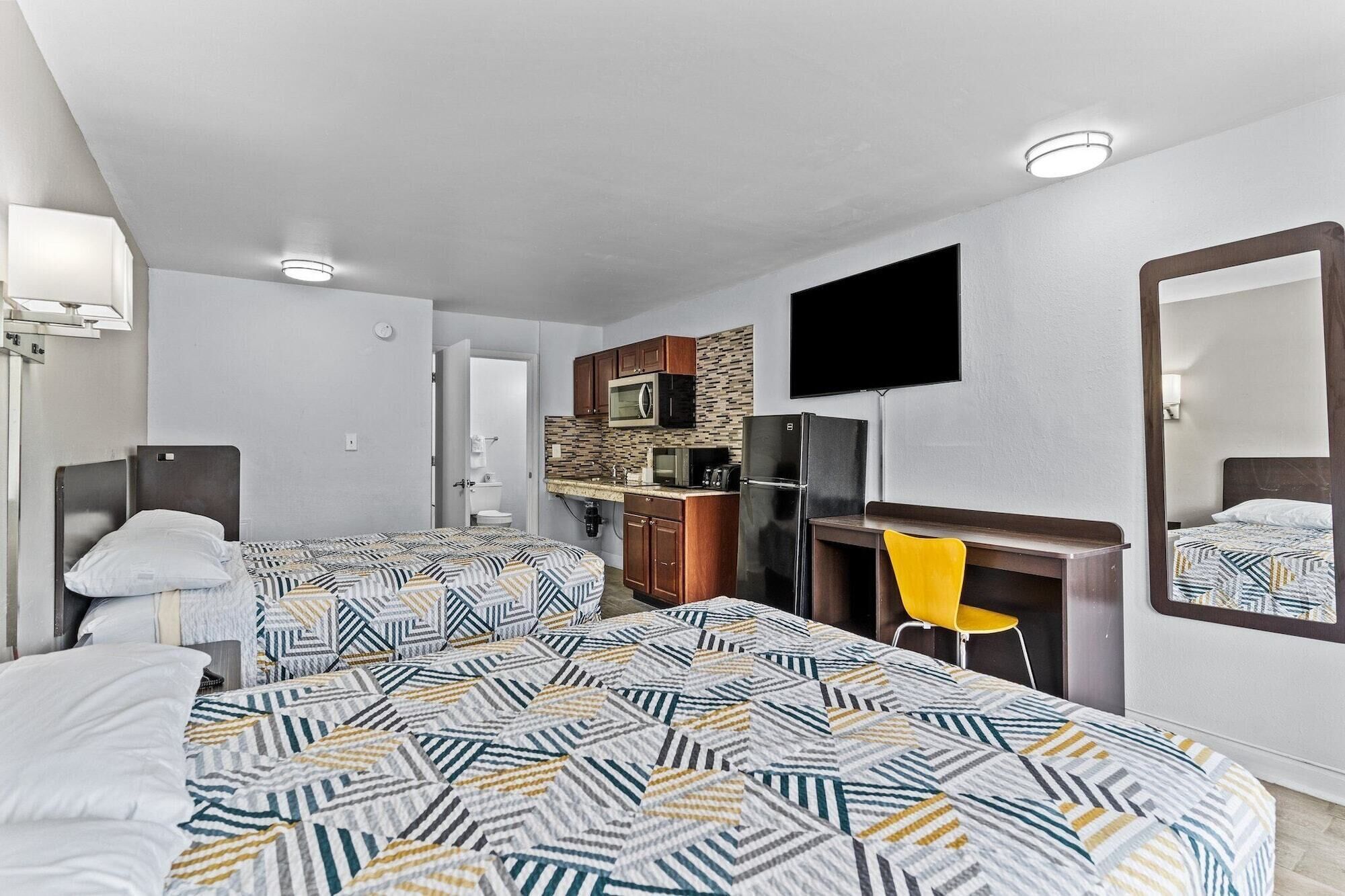 A hotel room with two beds, a kitchenette, a TV, and a bathroom visible through an open door.