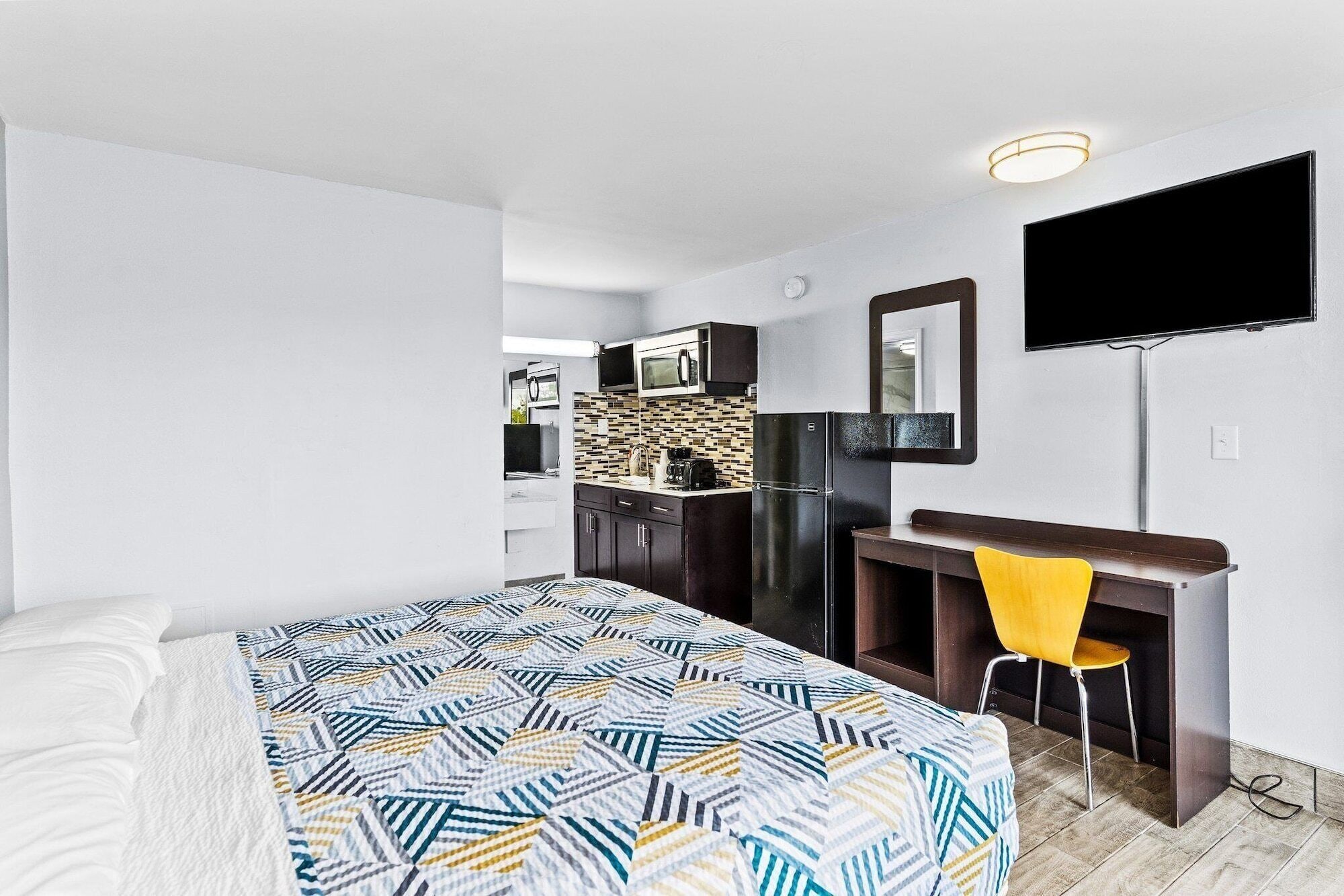 Une chambre d’hôtel compacte comprenant un lit, un bureau avec une chaise, un téléviseur à écran plat et une kitchenette.