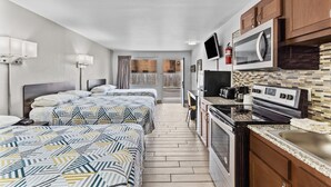 A compact hotel room with two beds, a kitchenette, a TV, and a view of the street. - Studio 6 Wilmington, NC (Wilmington)