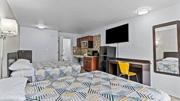 Une chambre d’hôtel avec deux lits, un bureau, une chaise, une télévision et une kitchenette.