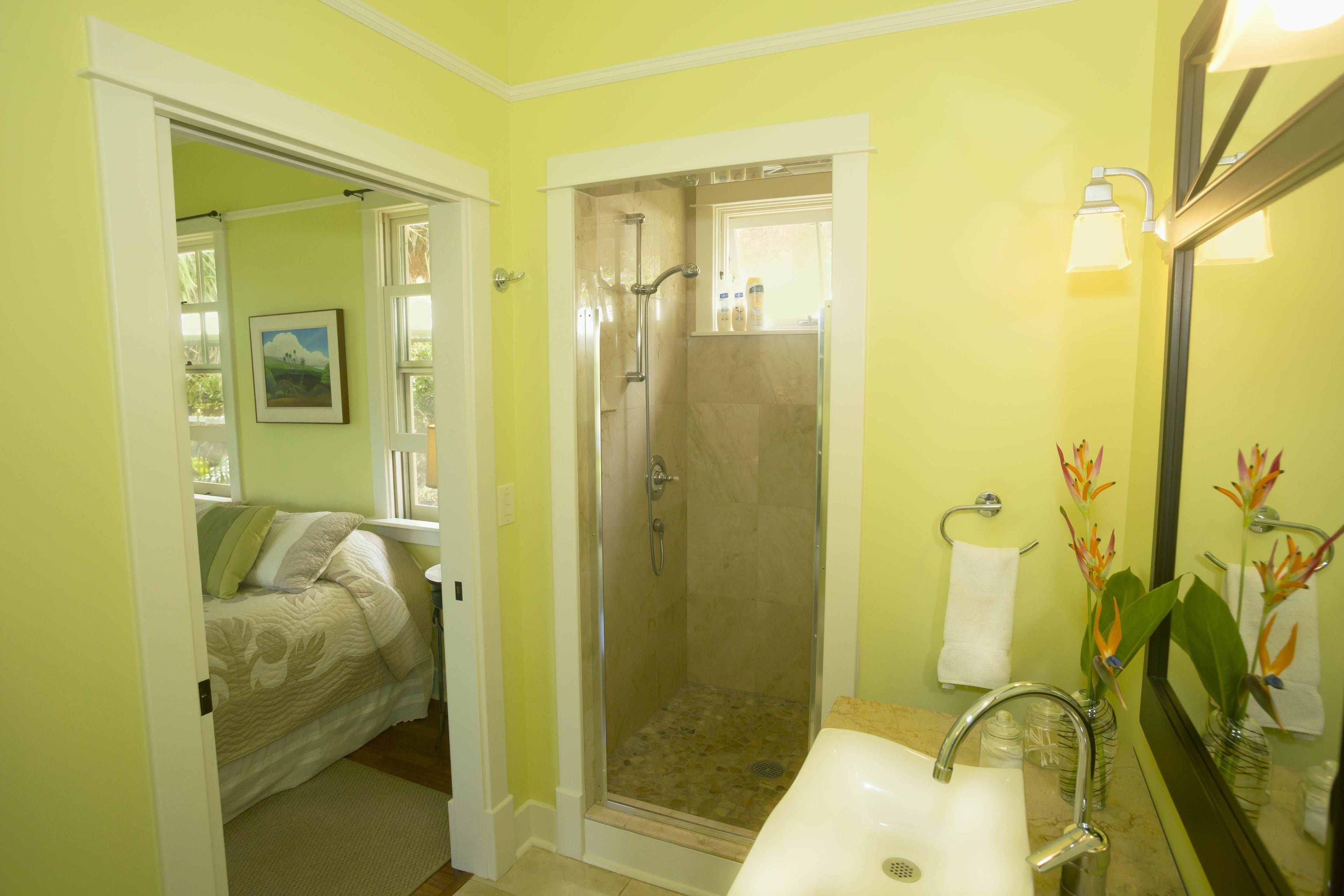 A bathroom with a shower, sink, and a bed visible through an open door.