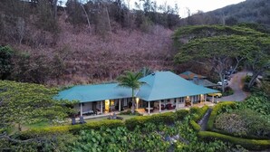 Um edifício de dois andares com telhado verde, cercado por vegetação exuberante e colinas.