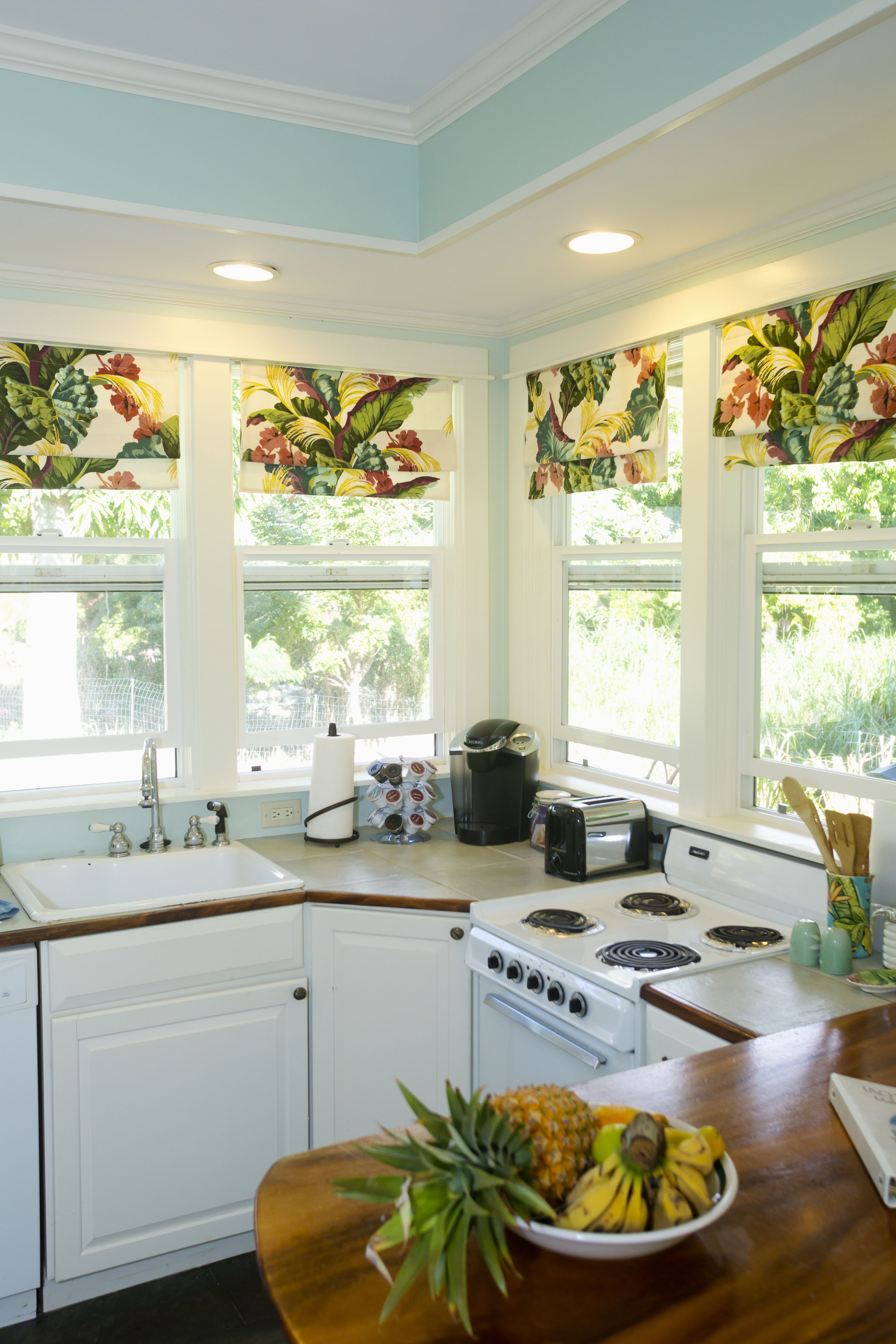 A kitchen with a white stove, a sink, and a window with floral curtains.