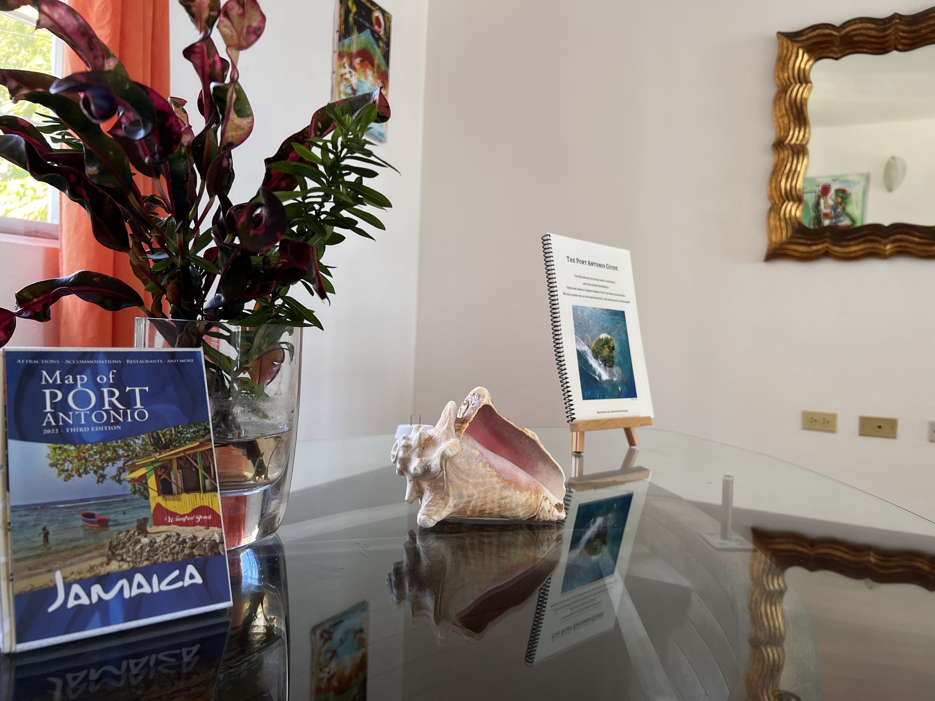 A glass table with a map of Port Antonio, a decorative shell, and a guidebook on a stand.