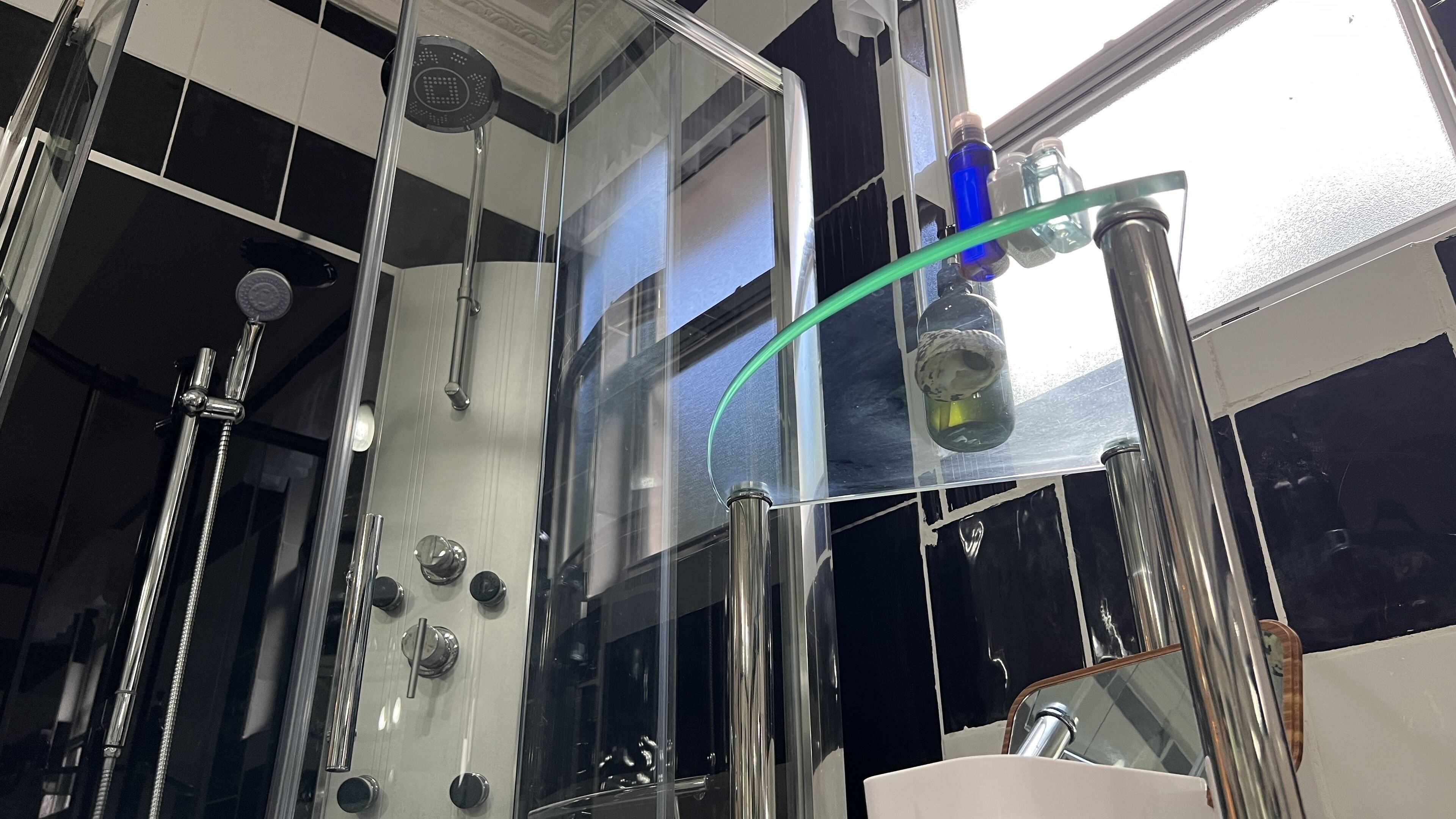 A modern bathroom with a glass-enclosed shower, multiple faucets, and a visible glass of water.