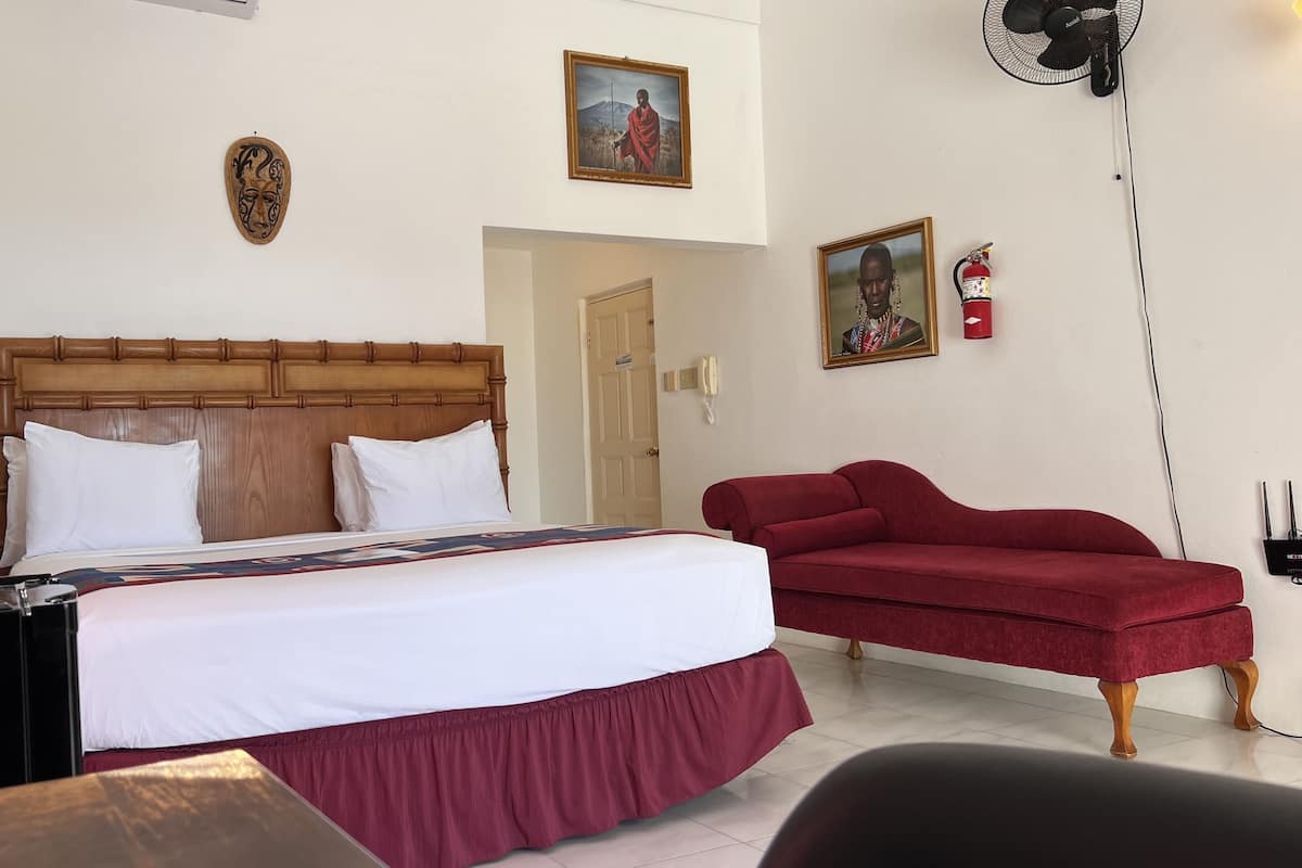 A hotel room with a wooden headboard bed, white bedding, a red sofa, and artwork on the walls.