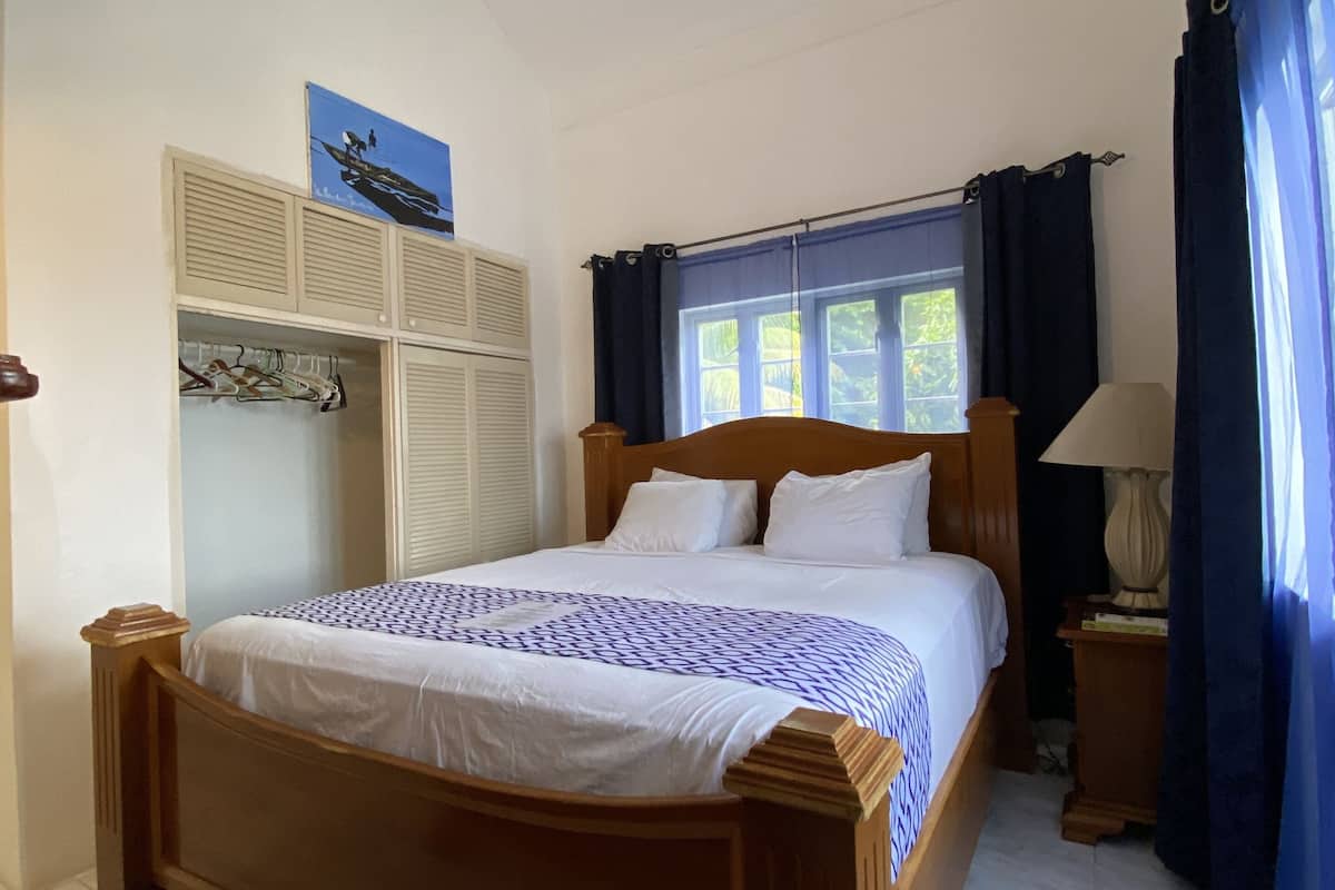A bedroom with a wooden bed, a wardrobe, a window with curtains, and a lamp.