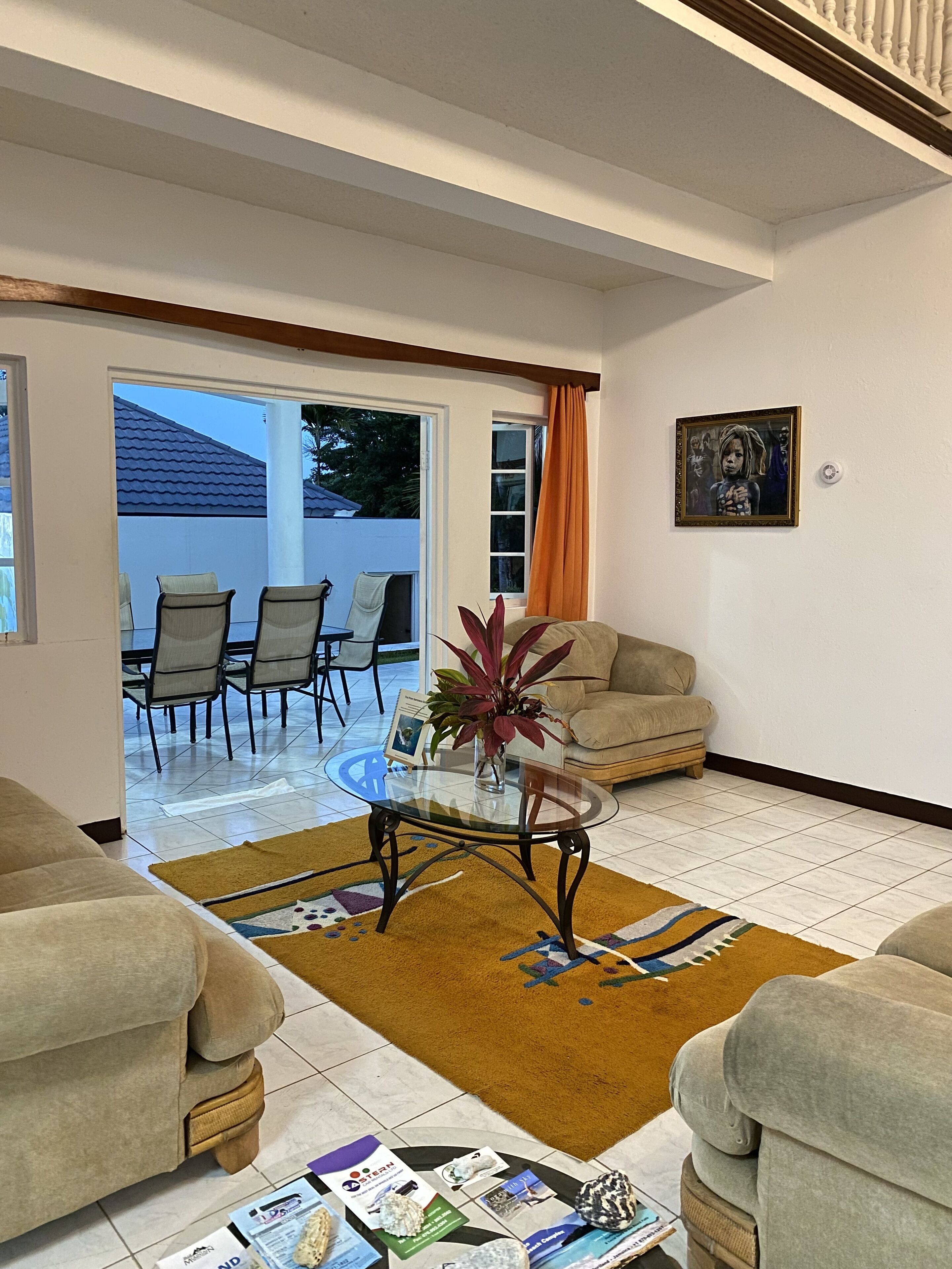 A living room with a glass coffee table, two sofas, a dining area with chairs, and a view of the outside.