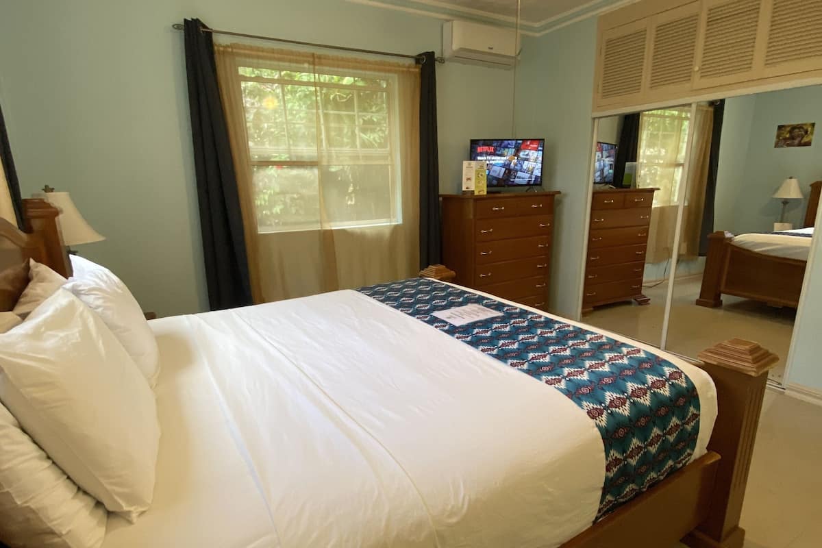 A bedroom with a bed, a ceiling fan, a television, a dresser, and a window with curtains.