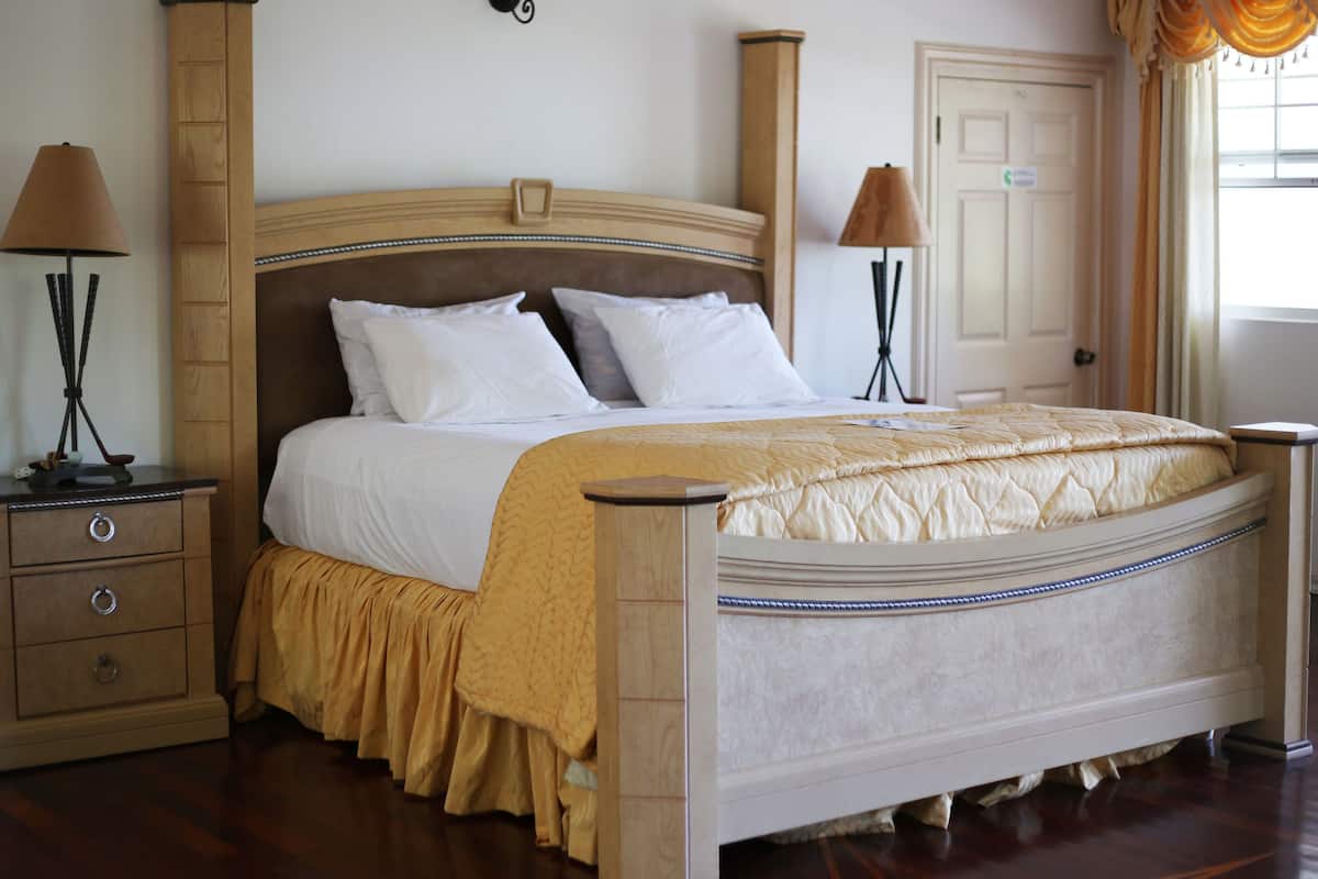 A neatly made bed with a wooden headboard, two bedside tables with lamps, and a door in the background.