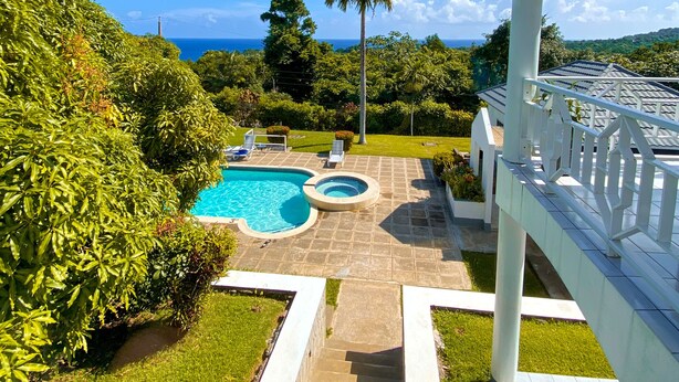 A pool area with a view of the ocean, surrounded by greenery and a white fence. - All Nations Guesthouse (Port Antonio)
