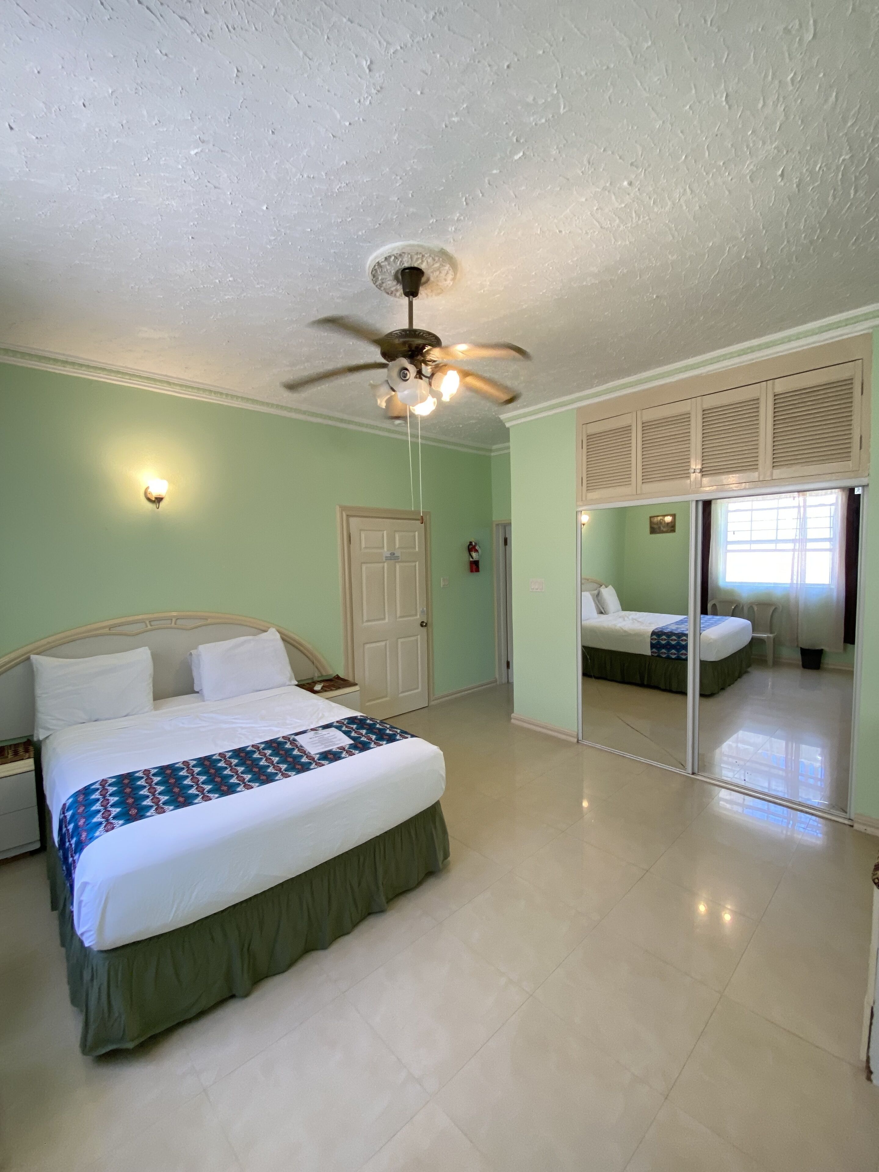 A bedroom with a bed, a ceiling fan, a door, and a sliding glass door leading to another room.