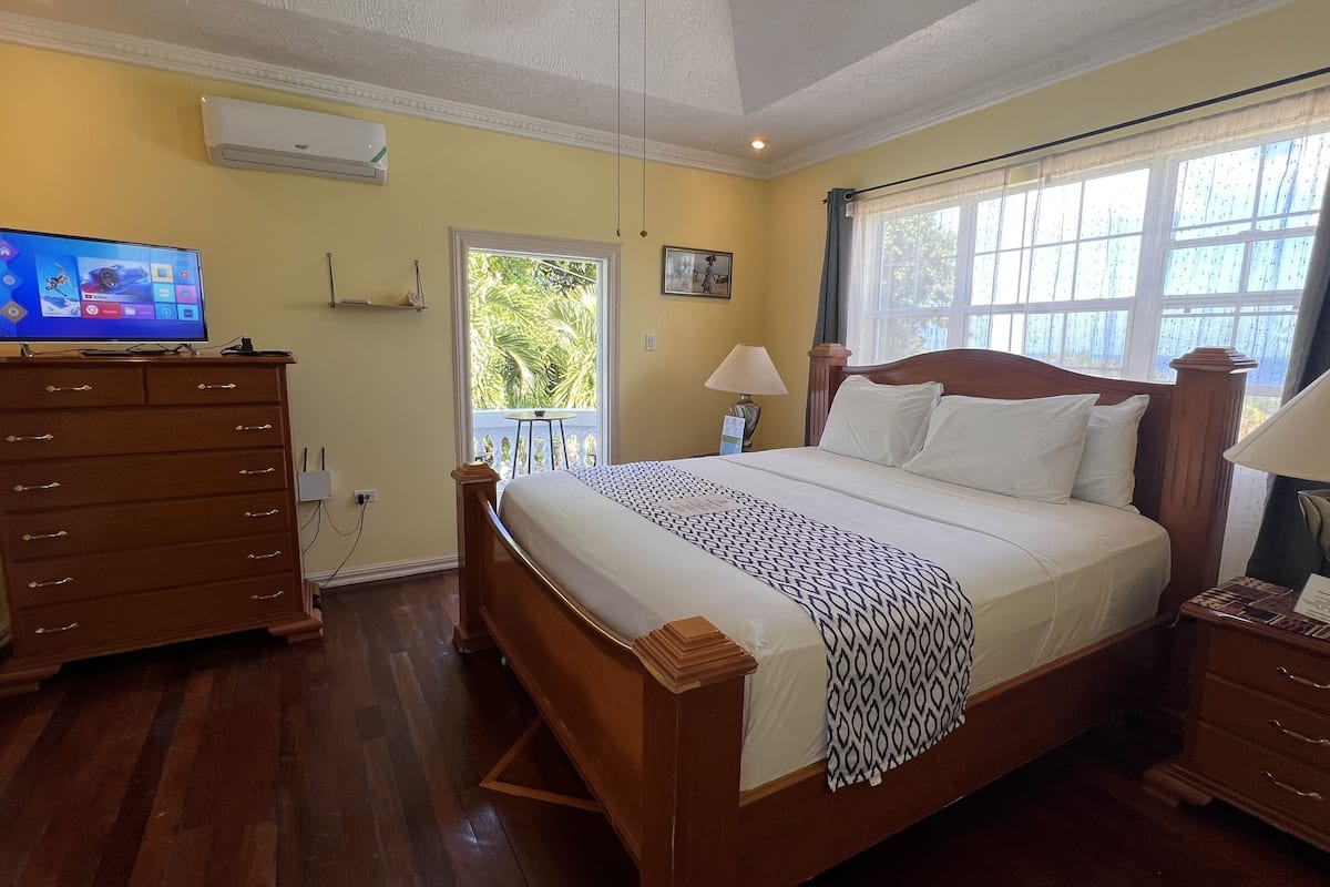 A bedroom with a wooden bed, a dresser, a television, and a window with curtains.