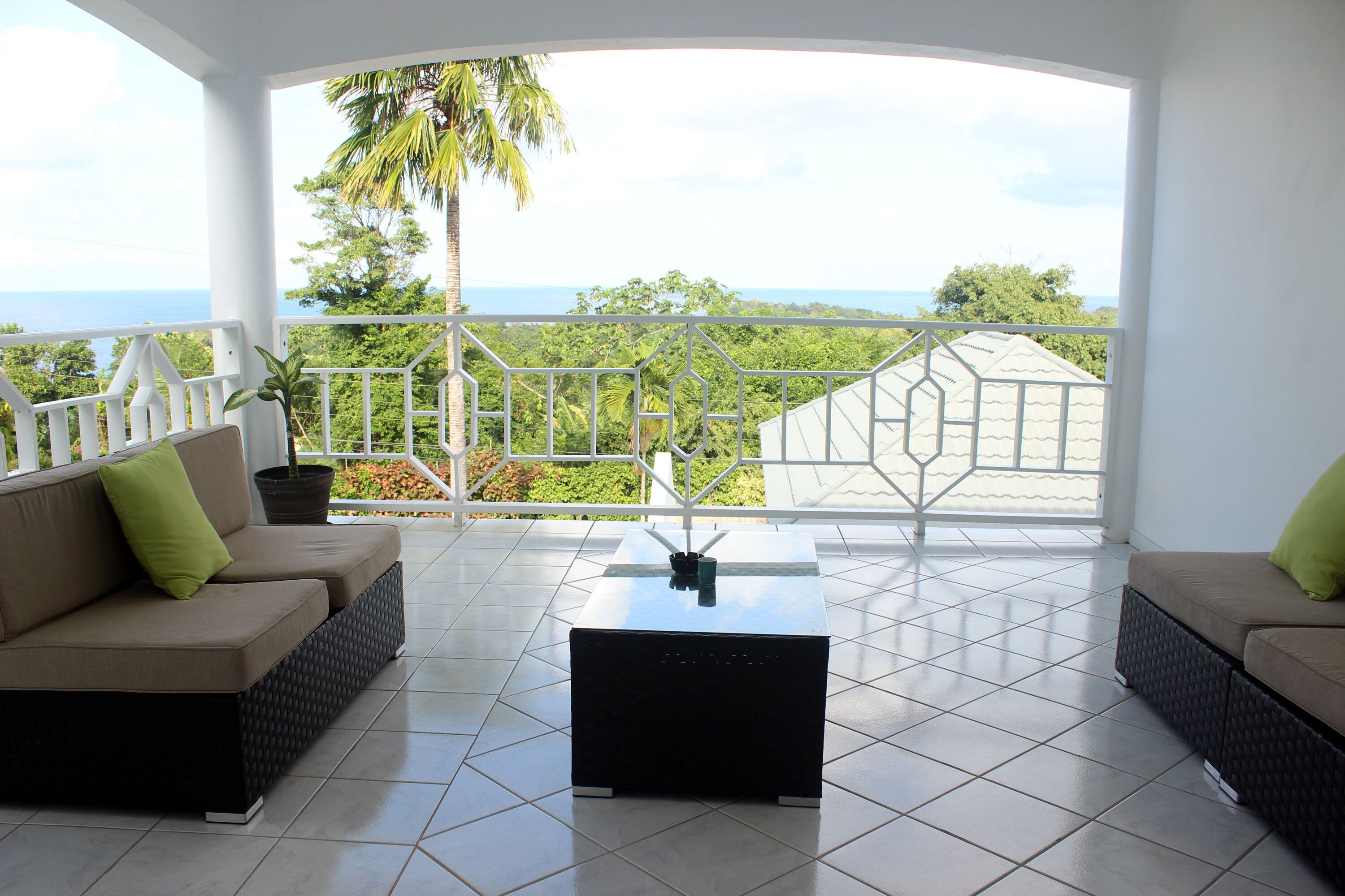 Un balcon avec vue sur l’océan, une balustrade blanche et une table noire.