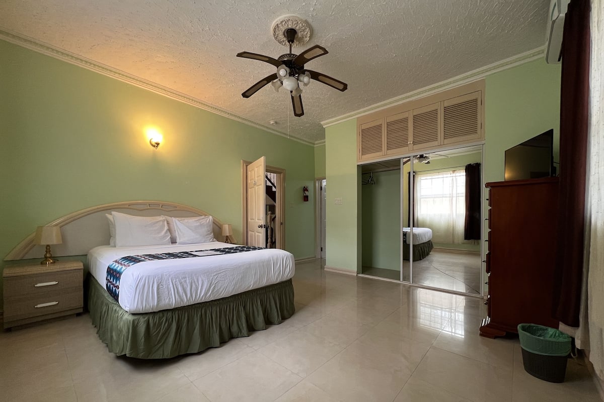 A bedroom with a bed, a nightstand, a ceiling fan, a wardrobe, and a sliding door leading to another room.