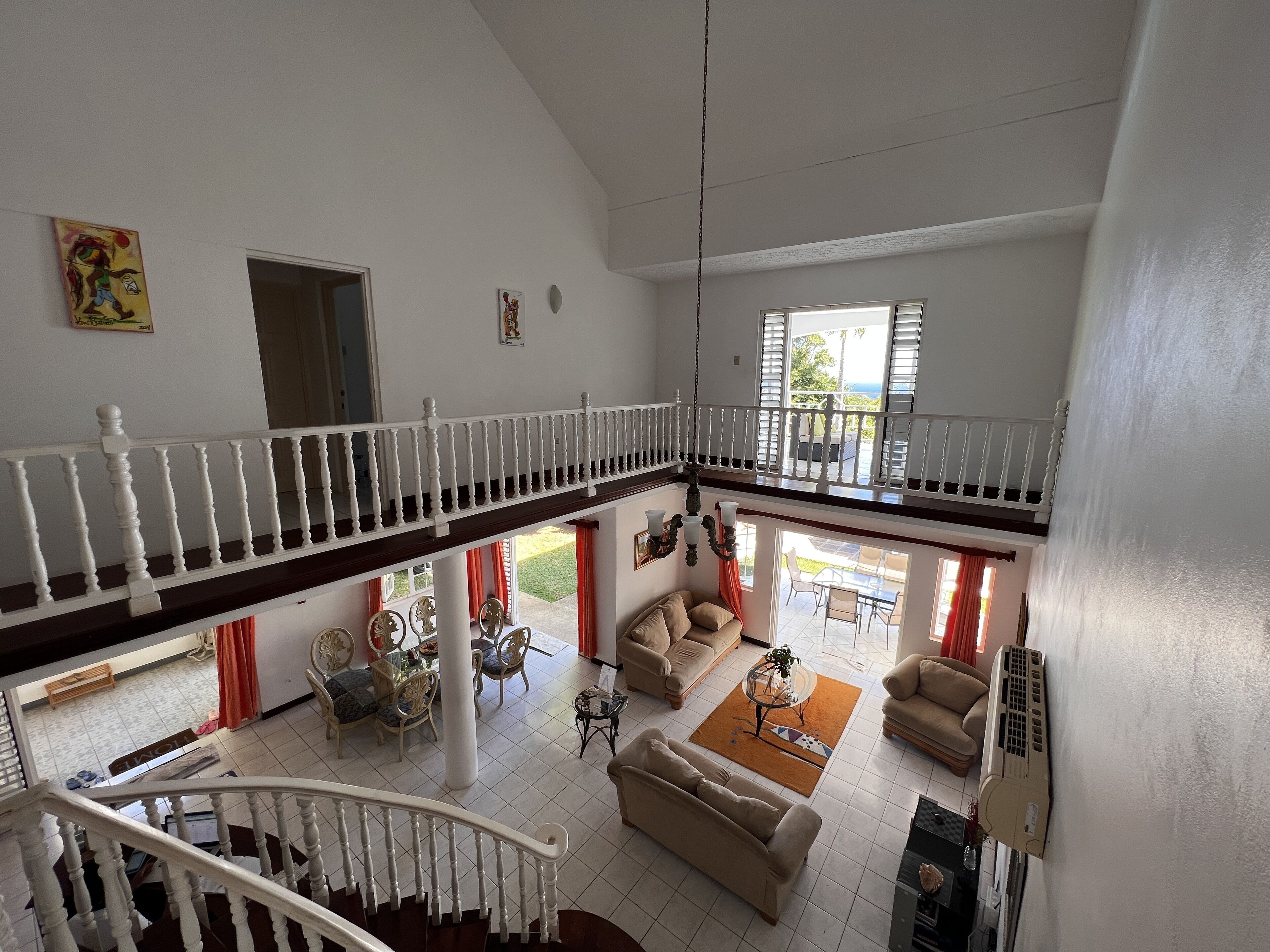 A spacious living area with a high ceiling, a staircase, and a balcony overlooking a garden.