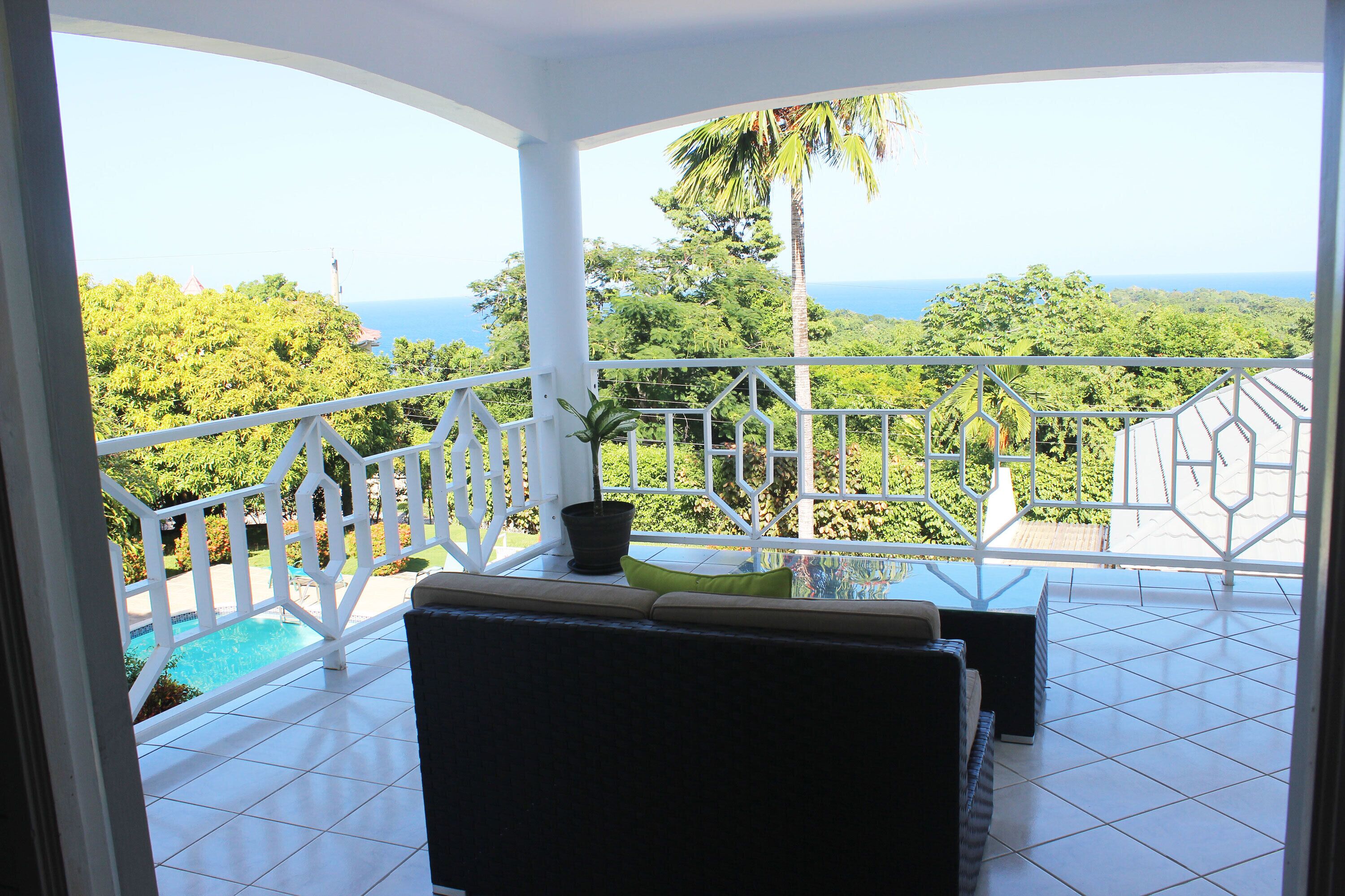A balcony with a view of the ocean, a pool, and lush greenery.