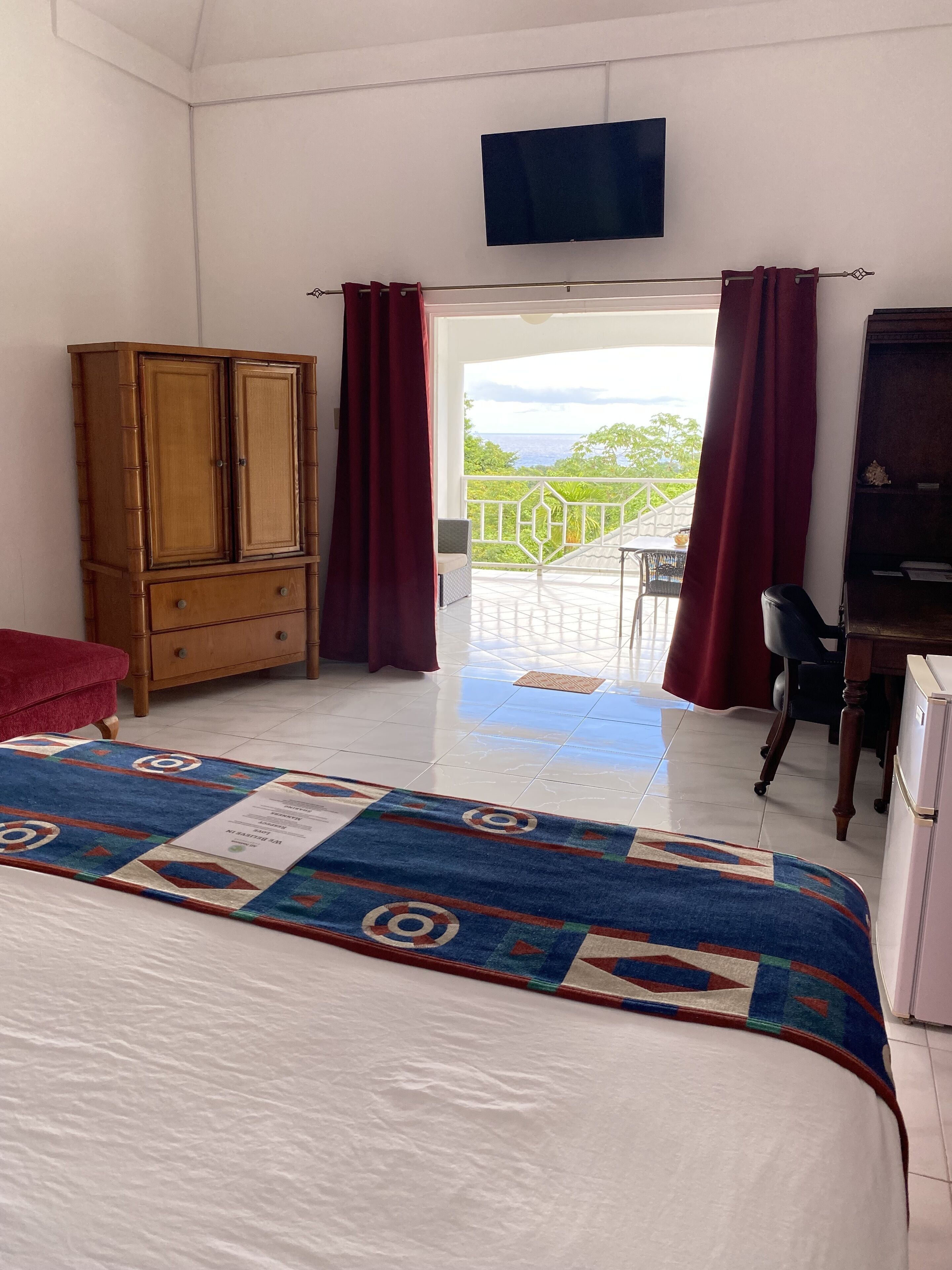 Un dormitorio con cama, armario de madera, escritorio y vista al exterior.