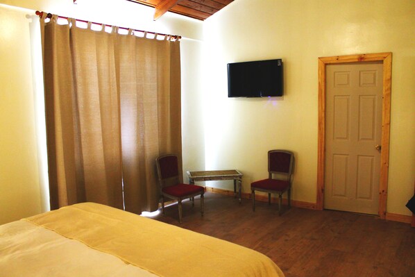 A hotel room with a bed, two chairs, a small table, a TV mounted on the wall, and a door. - Hotel Hoja de Parra (Santa Cruz)