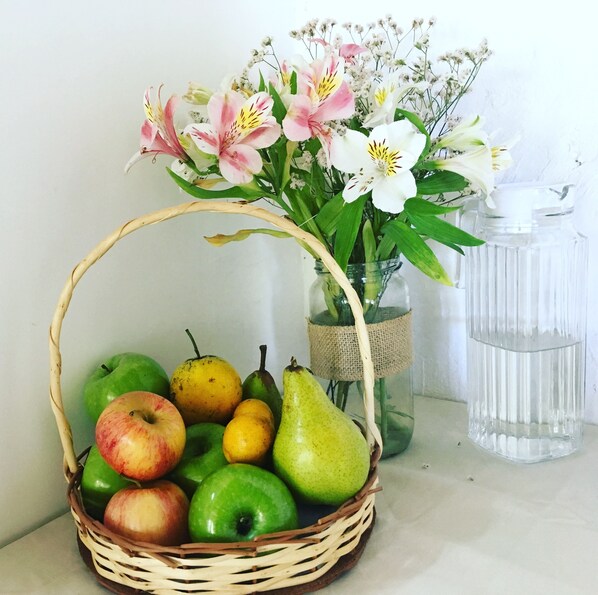 A wicker basket filled with green apples and pears, placed next to a vase with pink and white flowers. - Hotel Hoja de Parra (Santa Cruz)