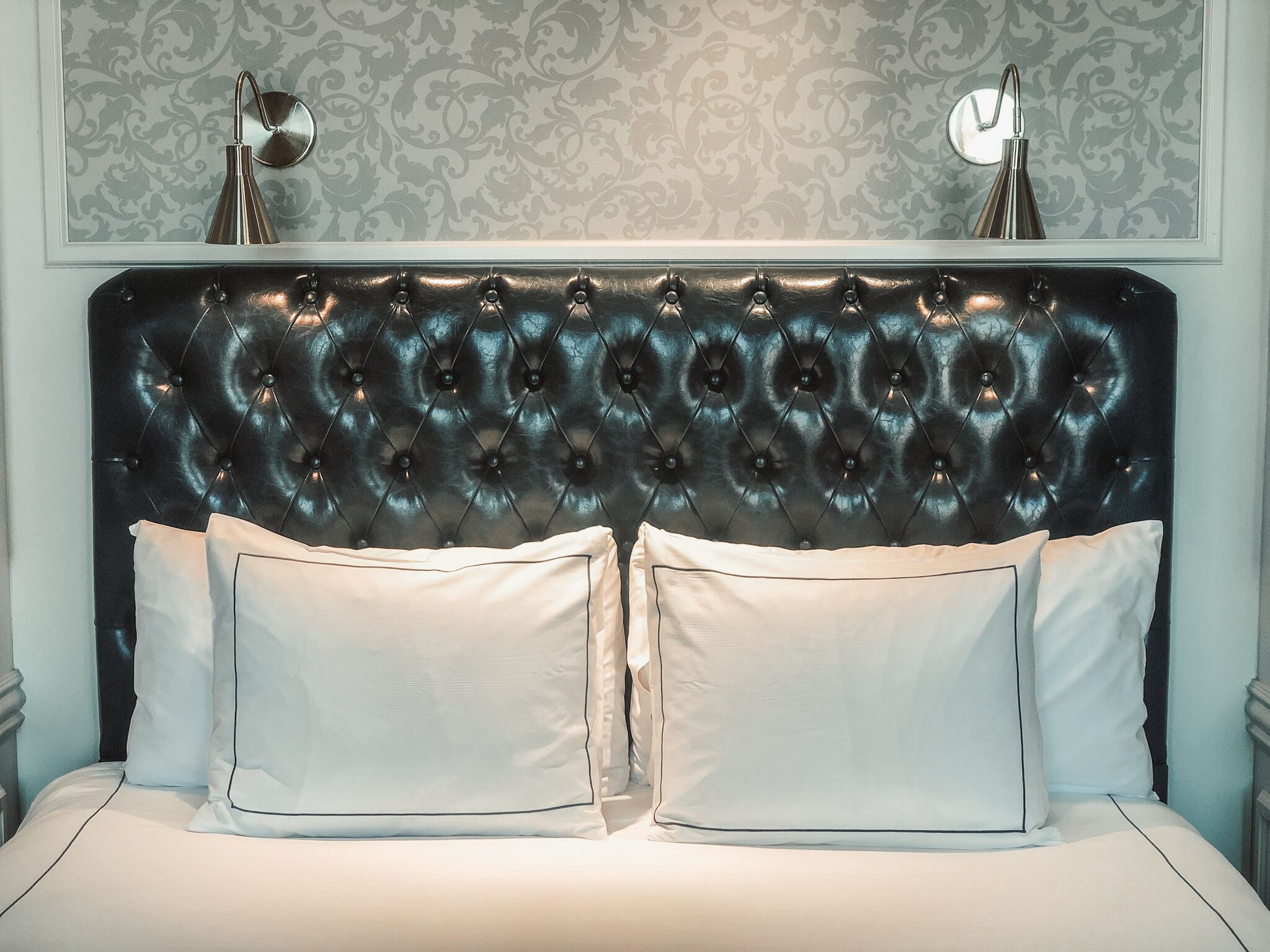 A bed with a tufted headboard, two bedside tables, and a patterned wallpaper.
