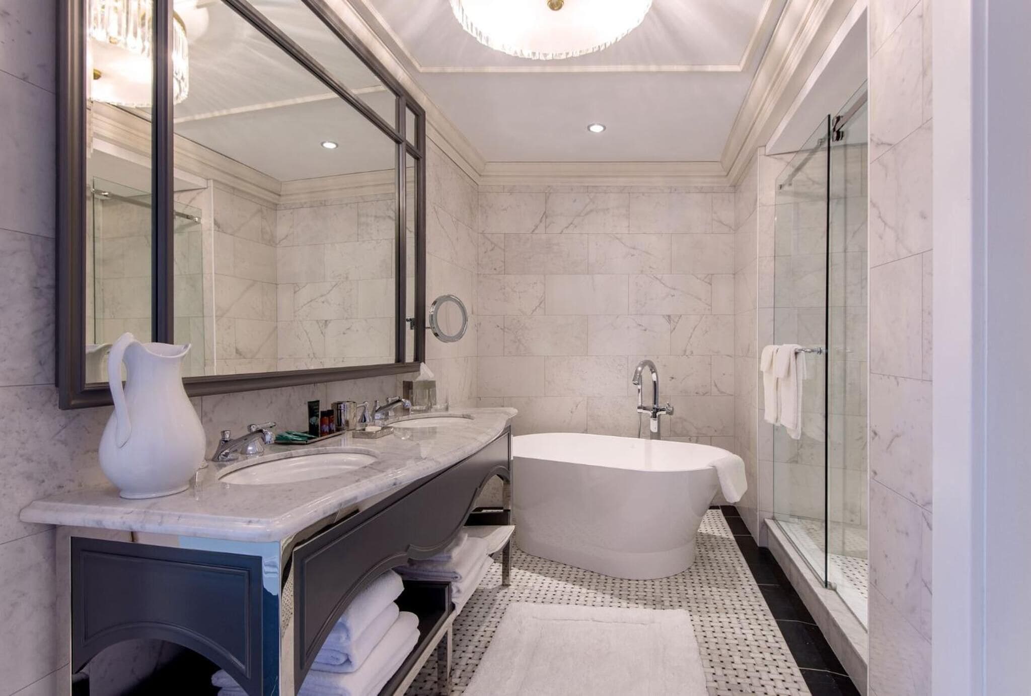 A modern bathroom with a large mirror, two sinks, a freestanding bathtub, and a glass shower enclosure.