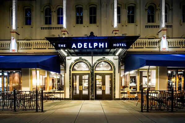 The exterior of The Adelphi Hotel with a grand entrance, a covered outdoor seating area, and a classic architectural style.
