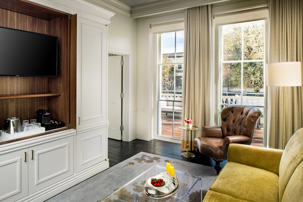 A modern living room with a flat-screen TV mounted on a wooden wall, a coffee machine, and a tray with fruit and juice on a glass table. - The Adelphi Hotel (Saratoga Springs)