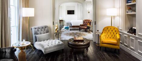 A hotel room with a tufted armchair, a yellow armchair, a grey tufted sofa, a wooden coffee table, and a patterned rug.