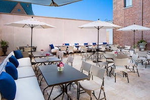 An outdoor patio with multiple tables and chairs, some with umbrellas, and a few potted plants.