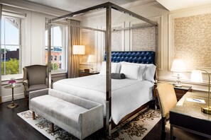 A four-poster bed with a tufted headboard, a sitting bench, and a desk with a lamp.