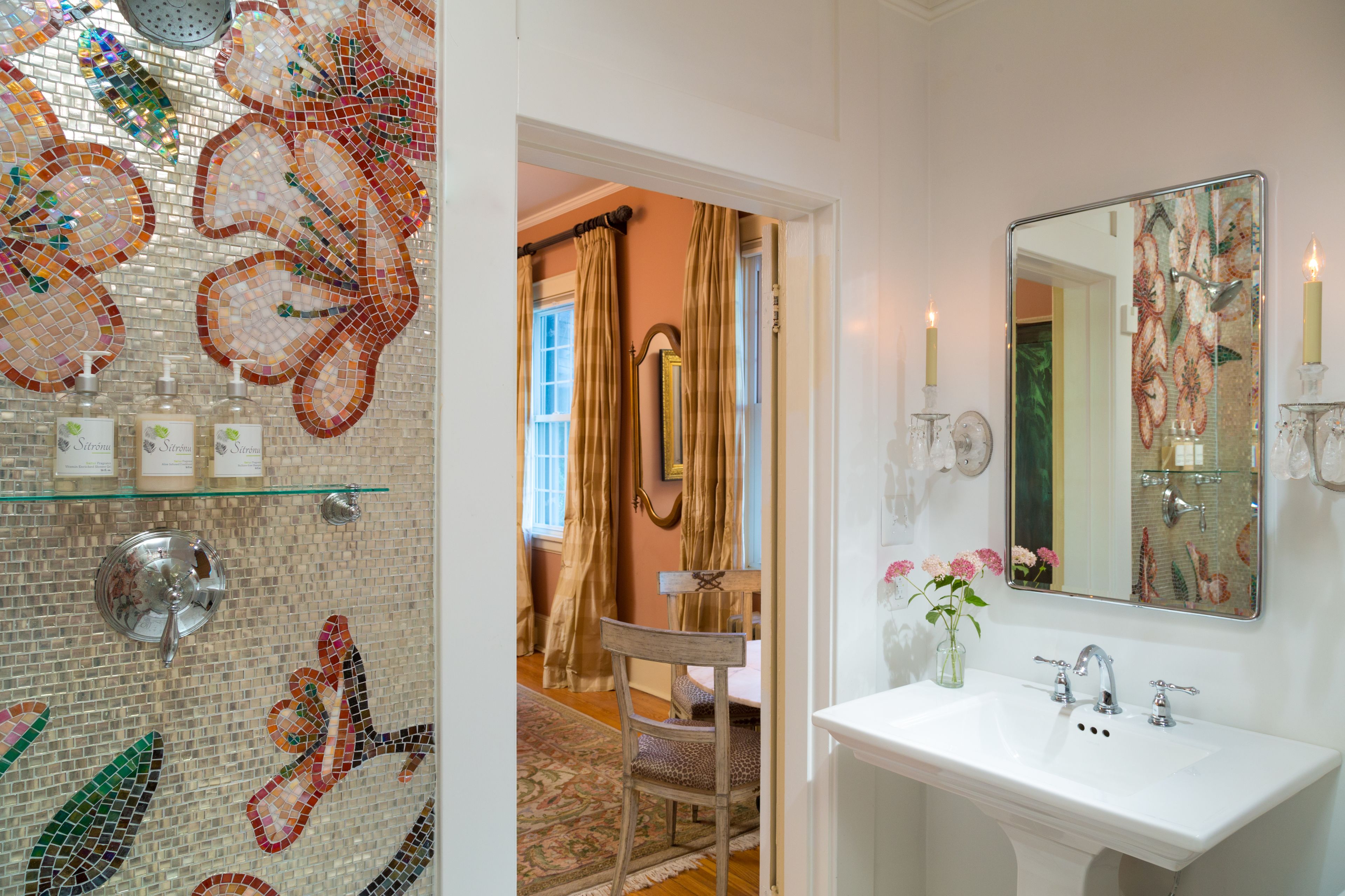 A bathroom with a mosaic wall, a white sink, and a mirror.