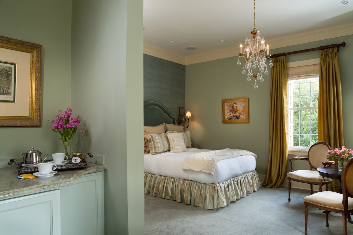 A bedroom with a bed, a dresser, a chandelier, and a window with curtains.