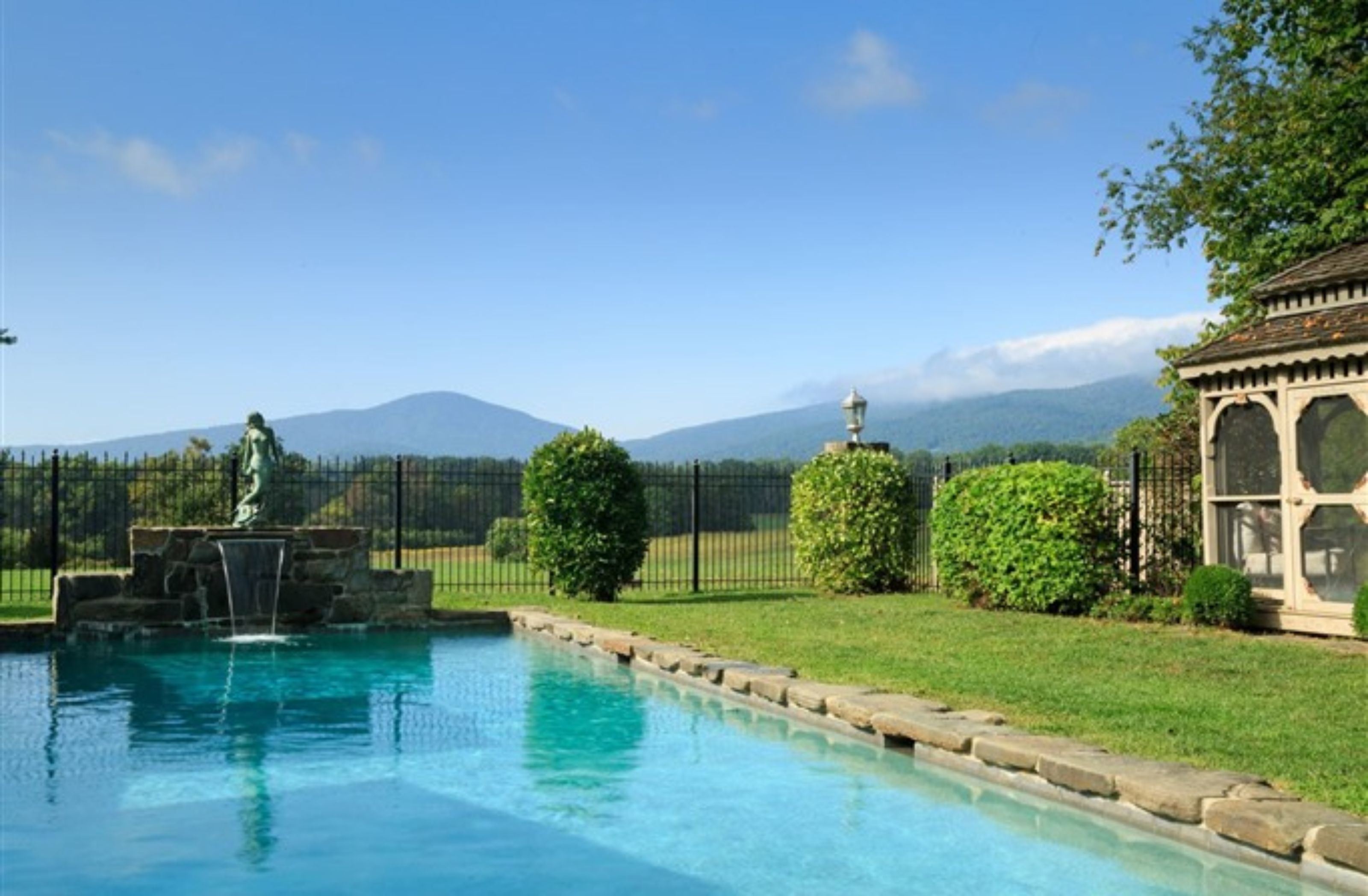 A swimming pool with a statue, a gazebo, and a view of mountains.