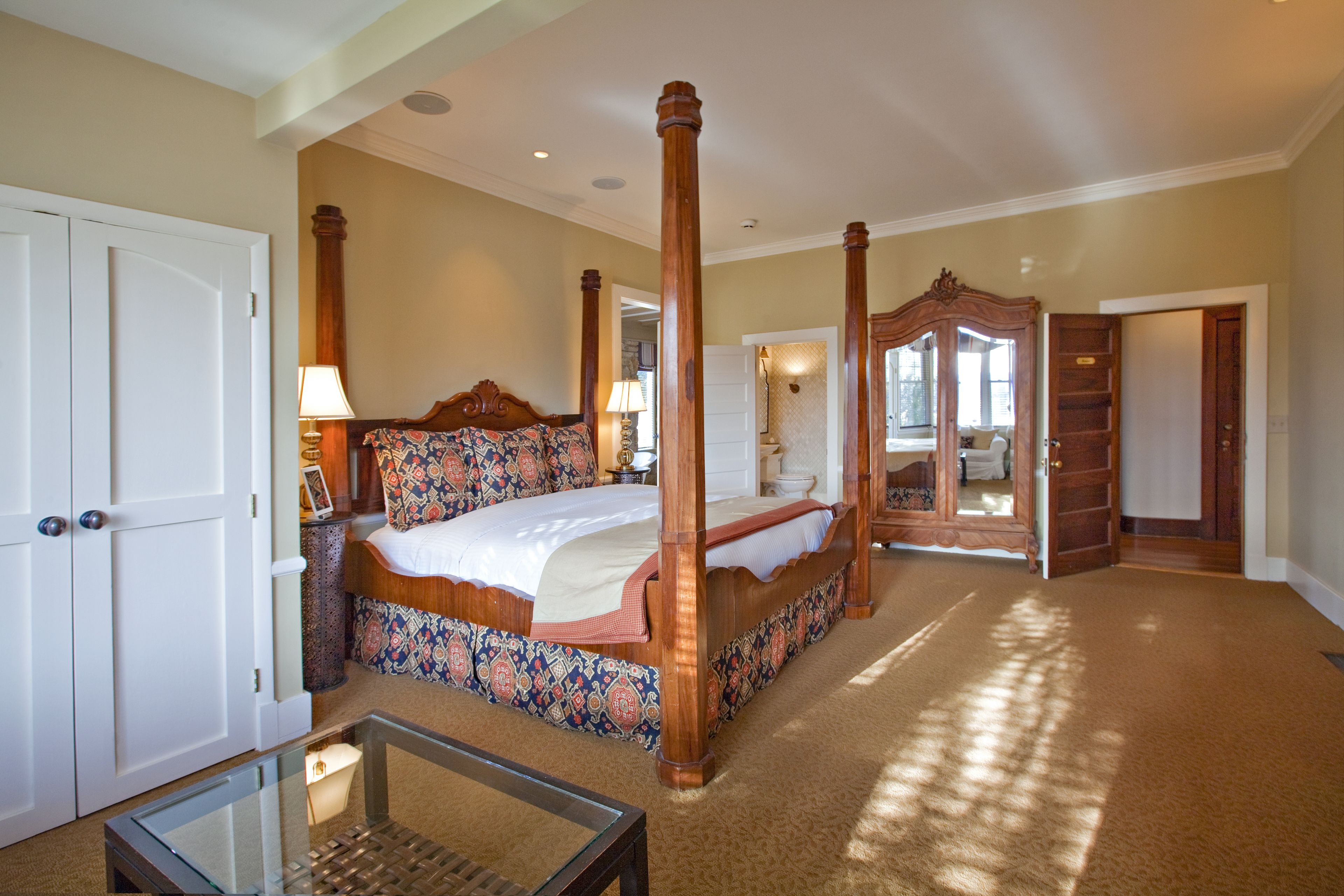 A spacious bedroom with a four-poster bed, a glass coffee table, and a walk-in closet.