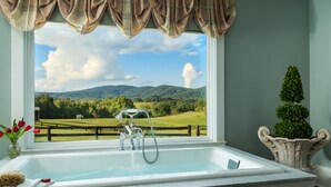A bathroom with a large window, a bathtub, and a view of a green landscape. - Glen Gordon Manor (Huntly)