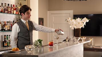 A bar area with a bartender preparing a drink, a wine glass, and a bottle of liquor on the counter.