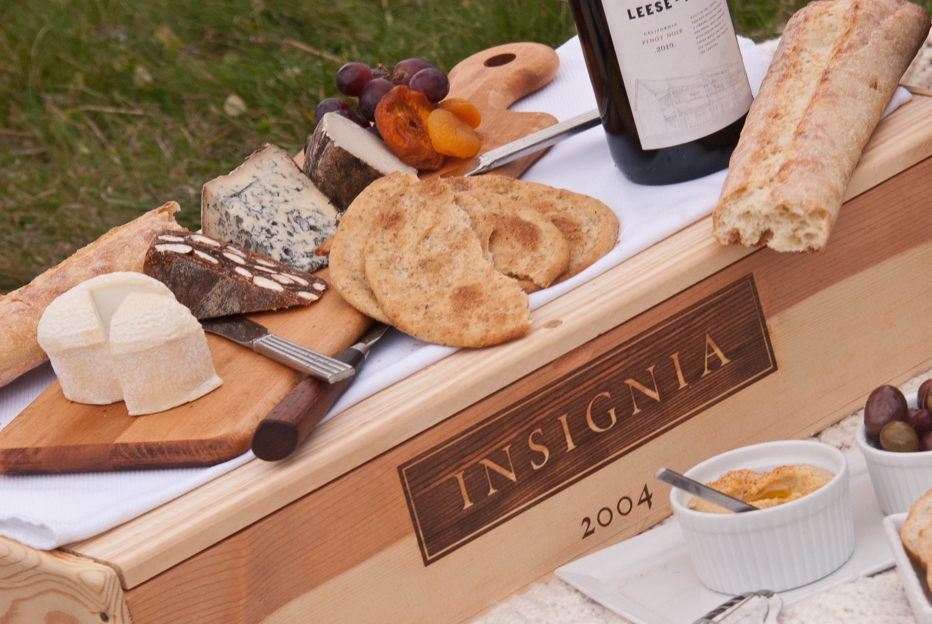 A charcuterie board with various cheeses, crackers, grapes, and a bottle of wine on a wooden table.