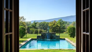 A view of a swimming pool with a fountain, surrounded by a fence and greenery, with mountains in the background. - Glen Gordon Manor (Huntly)