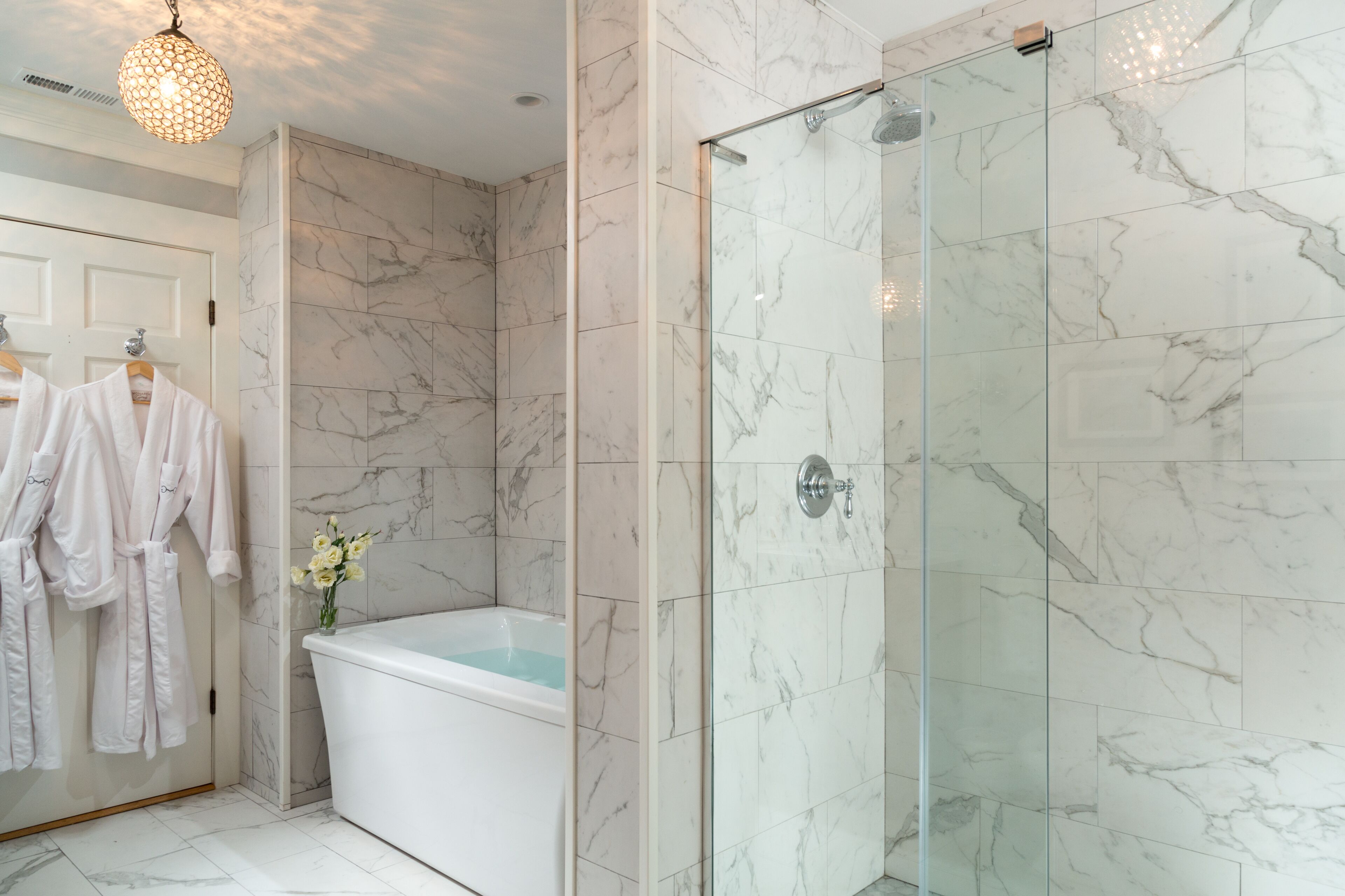 A modern bathroom with a glass-enclosed shower, a freestanding bathtub, and marble walls.