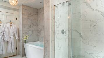 A modern bathroom with a glass-enclosed shower, a freestanding bathtub, and marble walls.