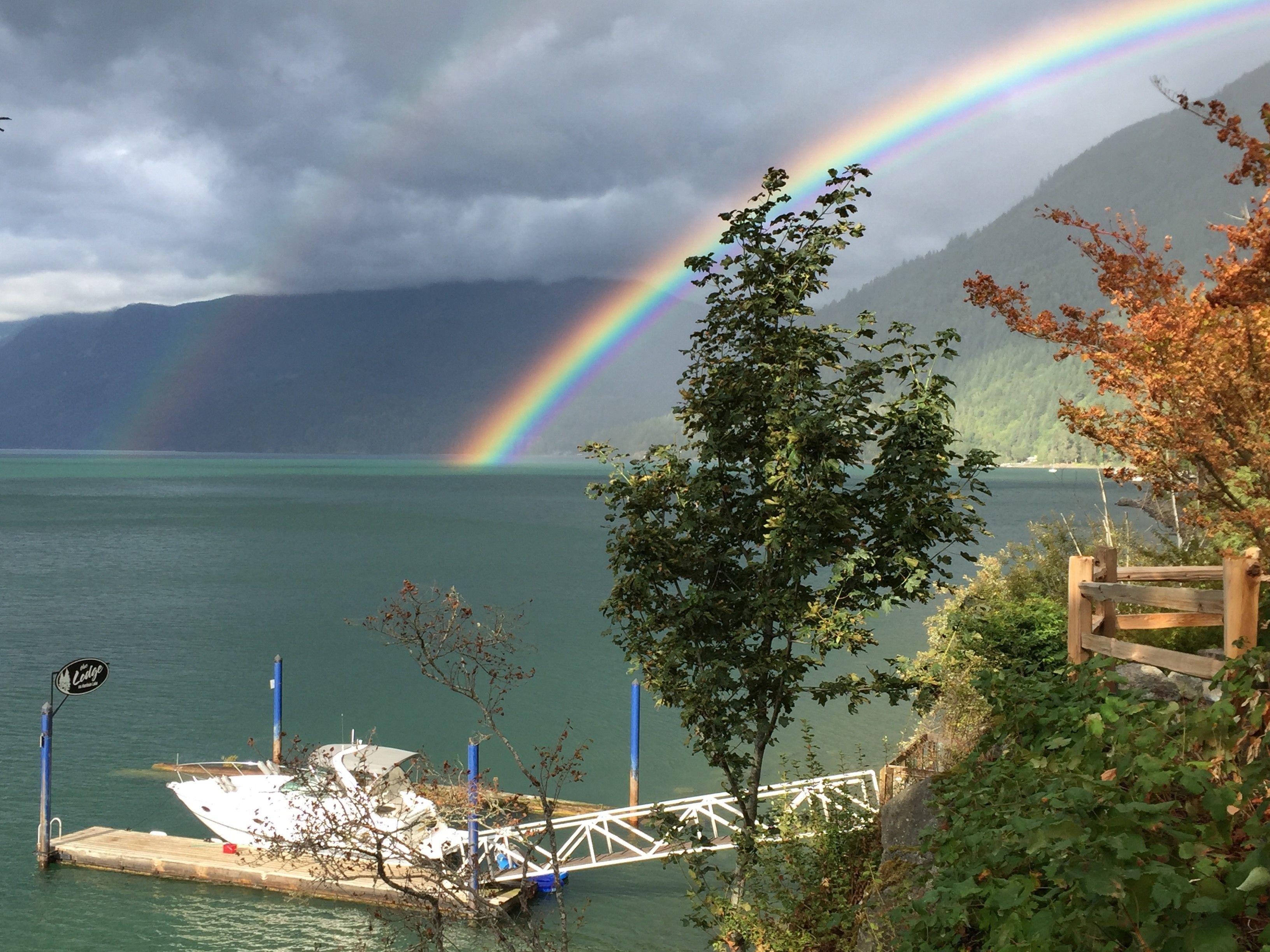 A dock with a boat, a rainbow, and mountains in the background.