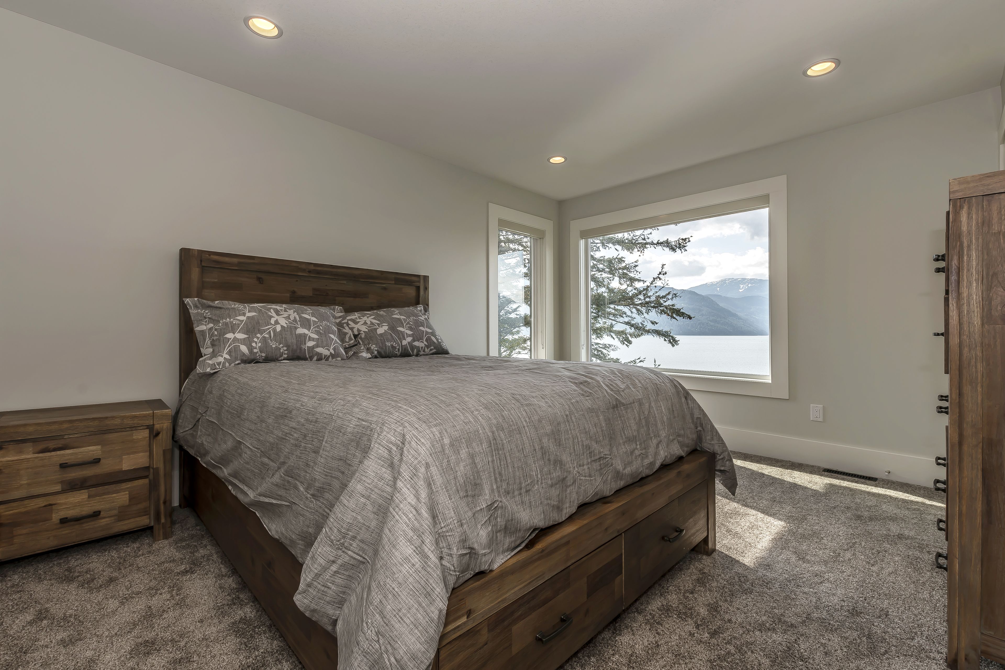 A bedroom with a large bed, a nightstand, a wooden wardrobe, and a window with a mountain view.