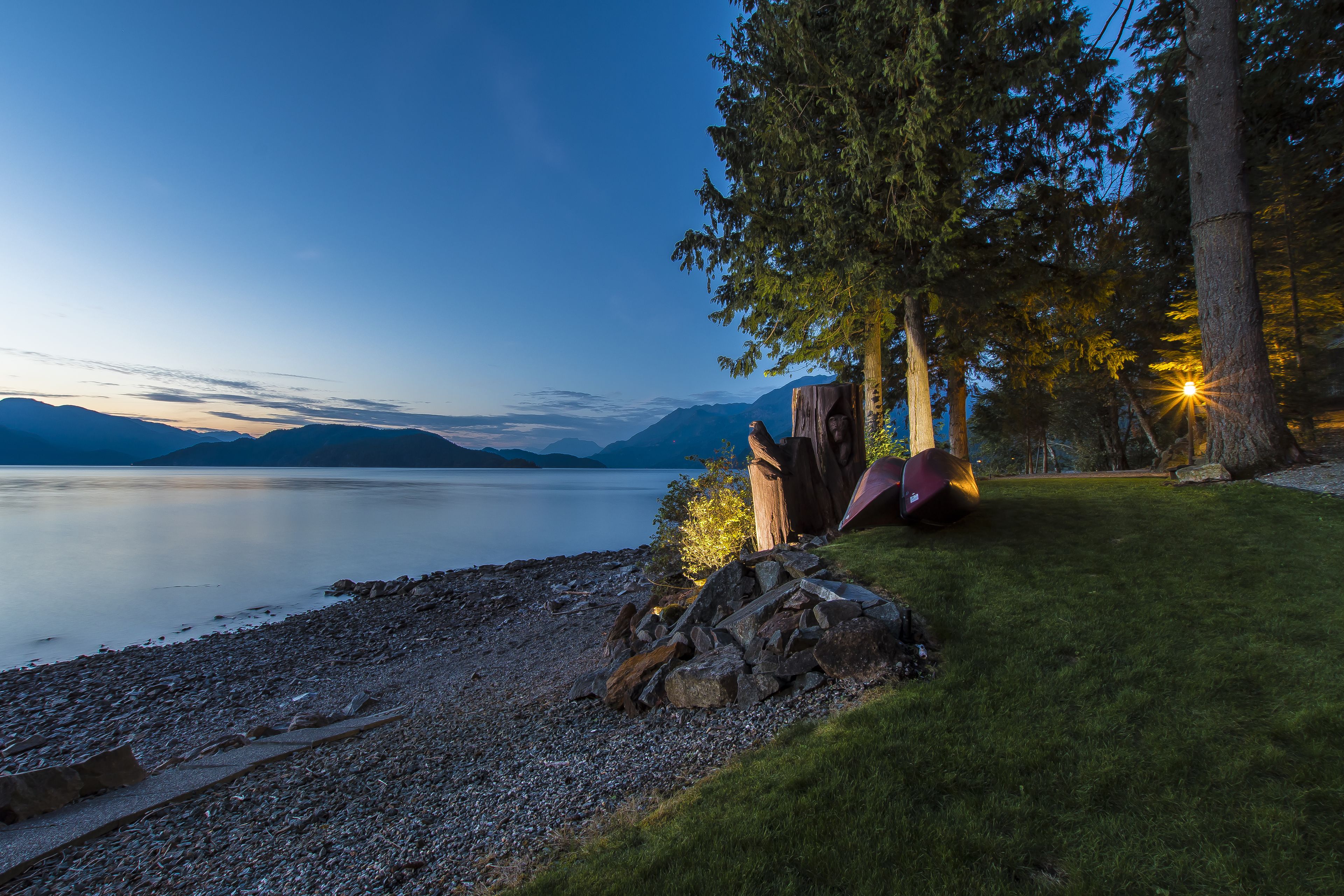 A lakeside scene with a grassy area, a tree stump, and a tent.