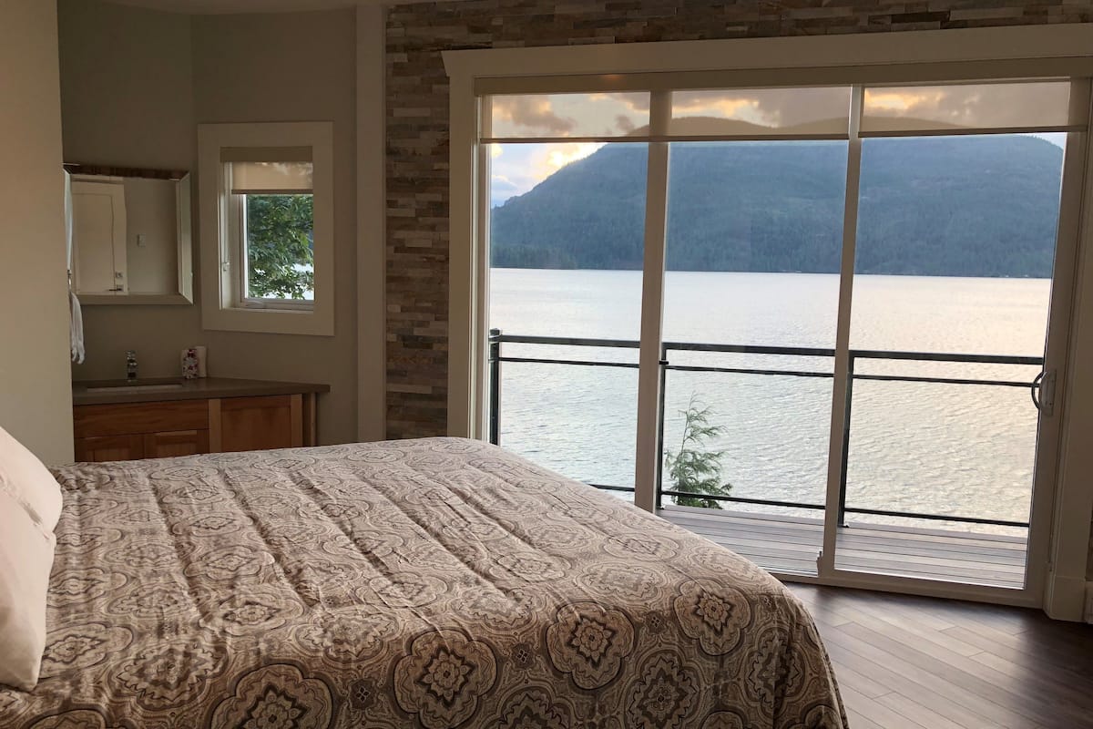 Ein Schlafzimmer mit einem großen Bett, ein Badezimmer mit Spiegel und Waschbecken sowie ein Balkon mit Seeblick und Bergblick.