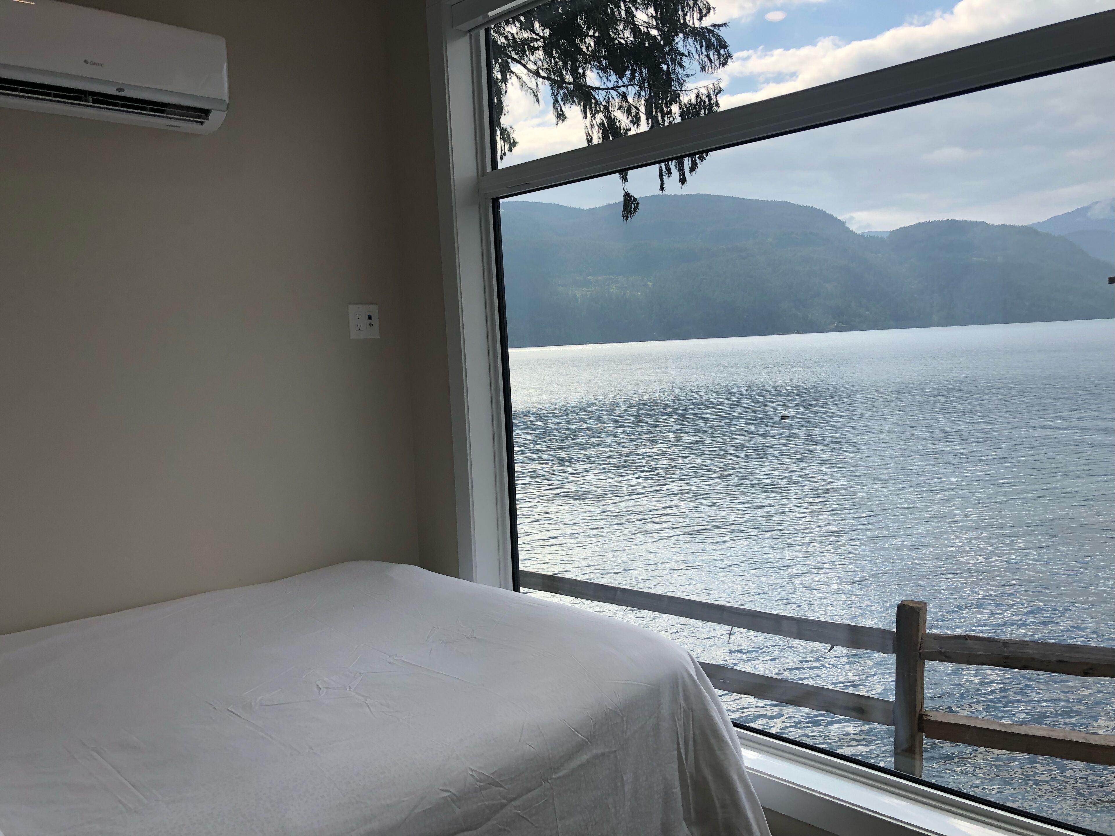 A room with a bed and a large window overlooking a lake with mountains in the background.