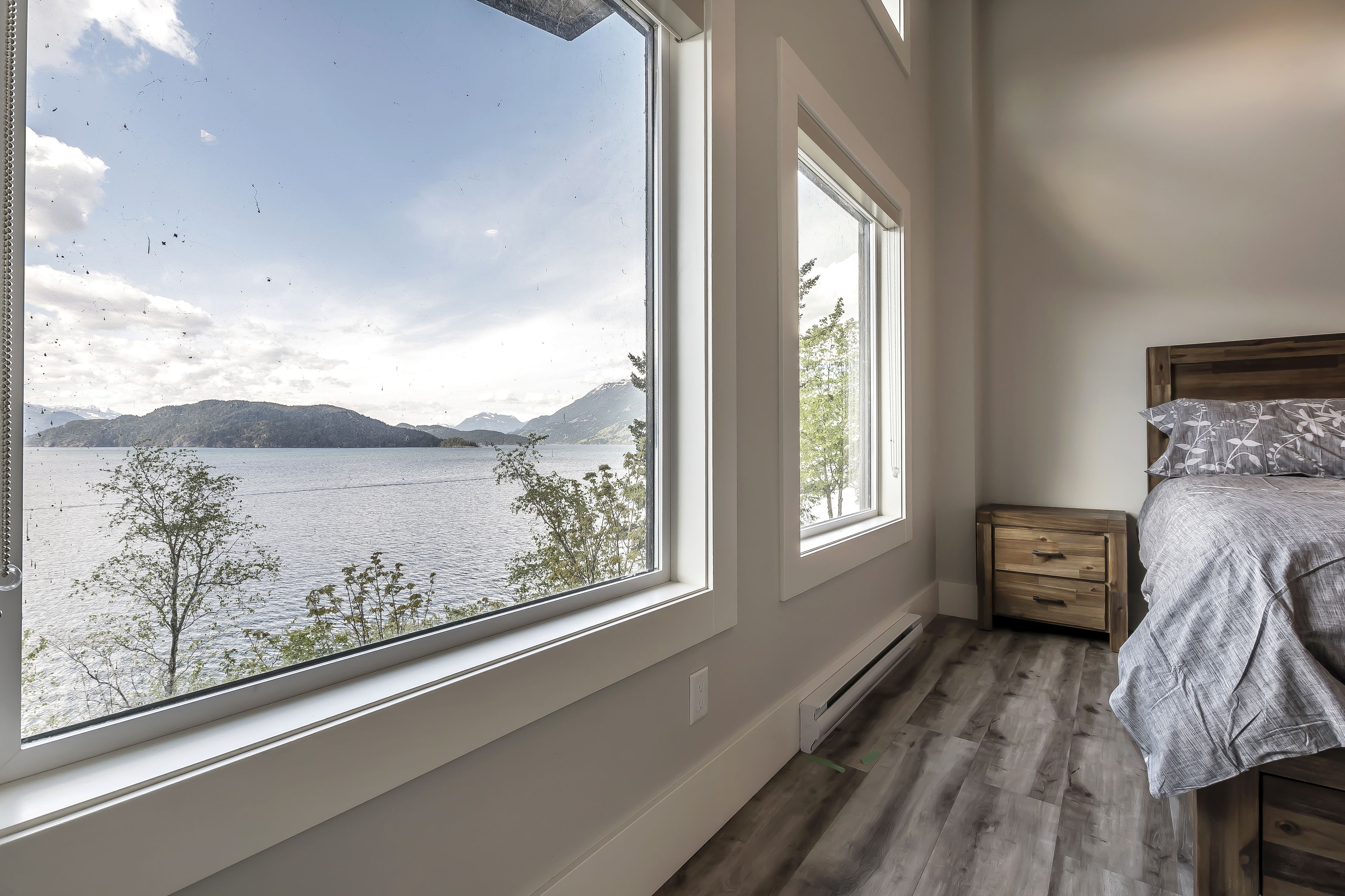 A bedroom with a large window offering a view of a lake and mountains.